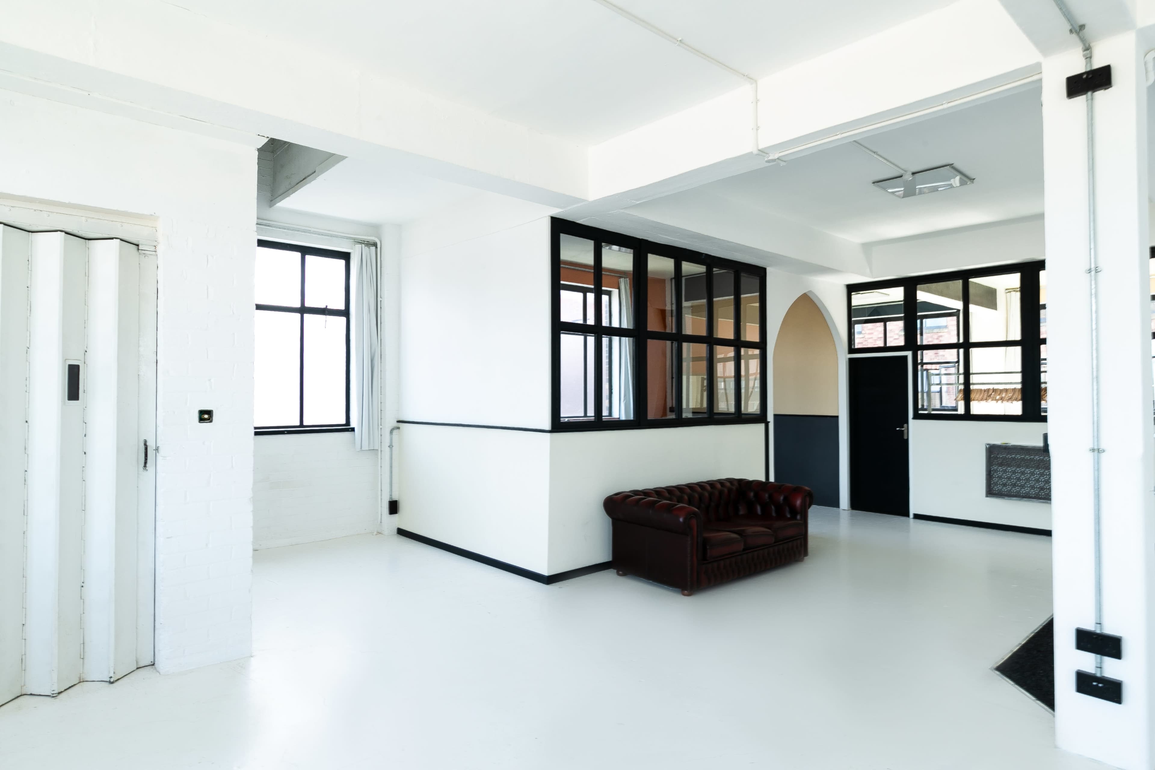A spacious, modern room with white walls, large windows, and a brown leather sofa.