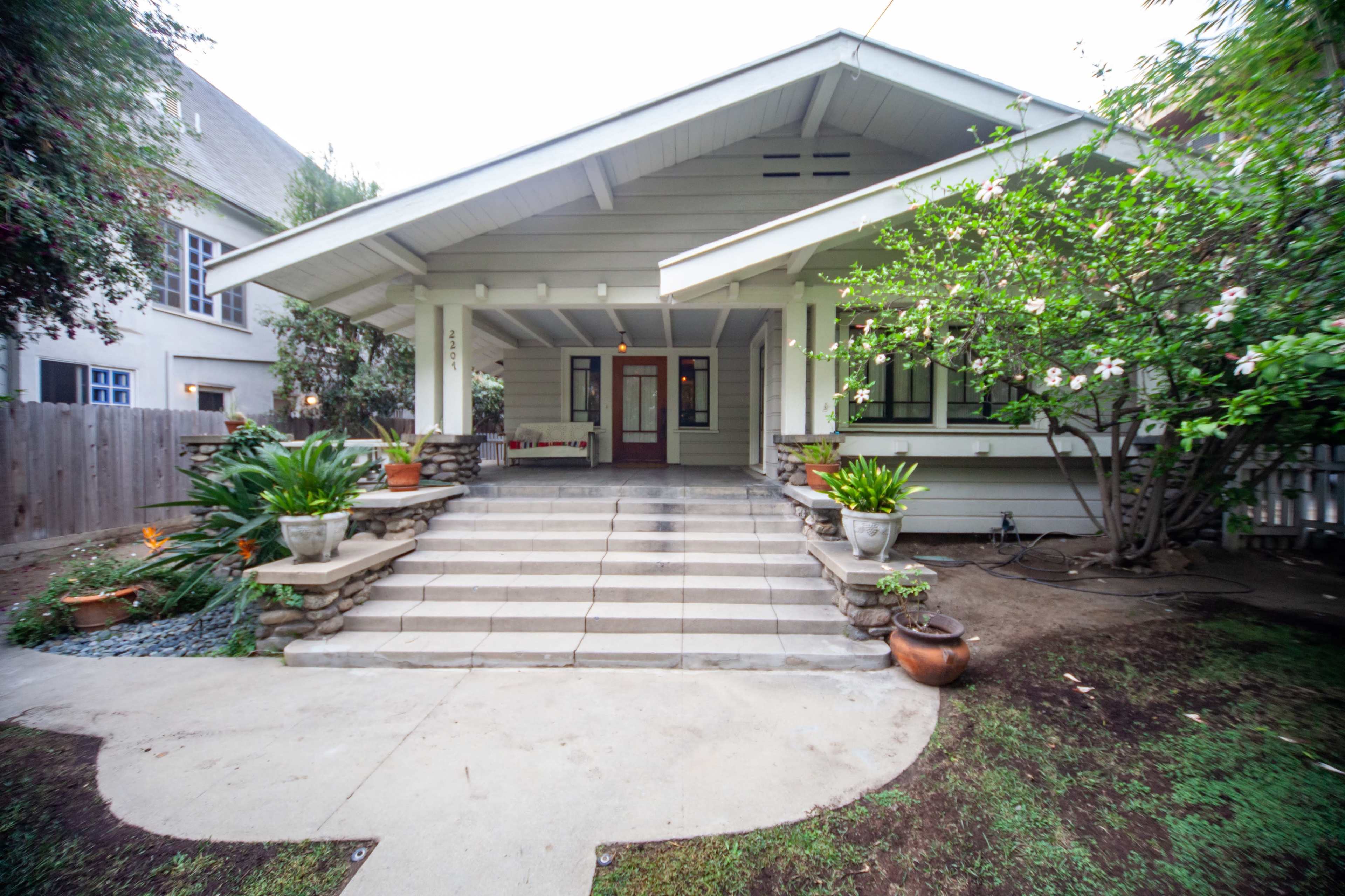 A house with a wide porch, flanked by potted plants and surrounded by a well-maintained garden.