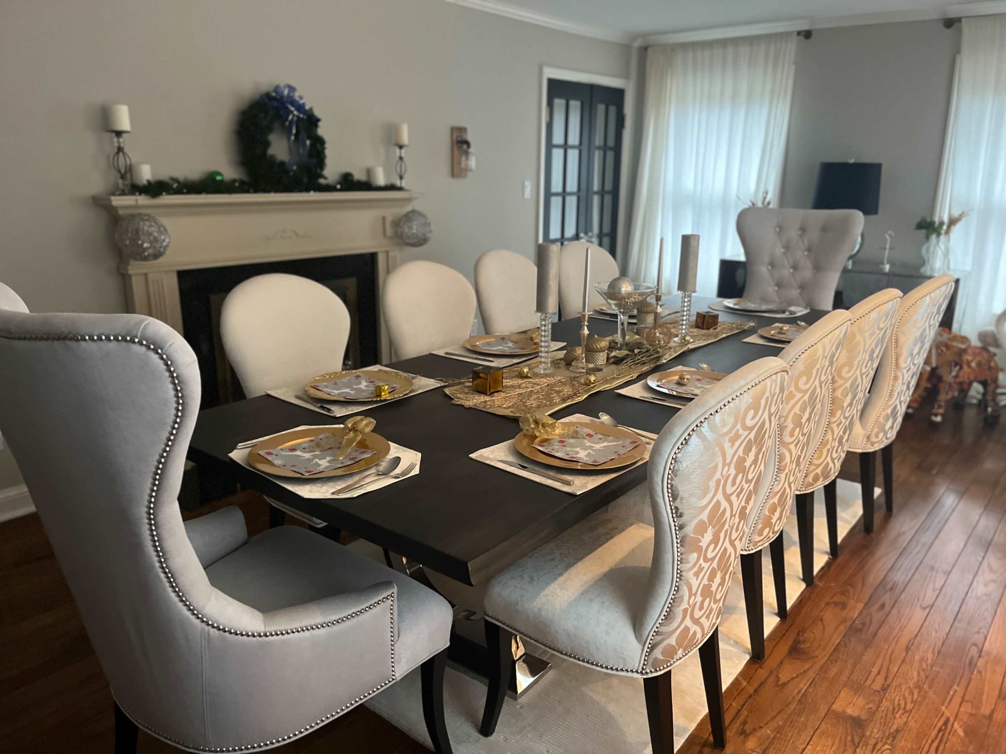 A dining table is set with elegant tableware and surrounded by upholstered chairs in a well-lit room featuring a fireplace and large windows.