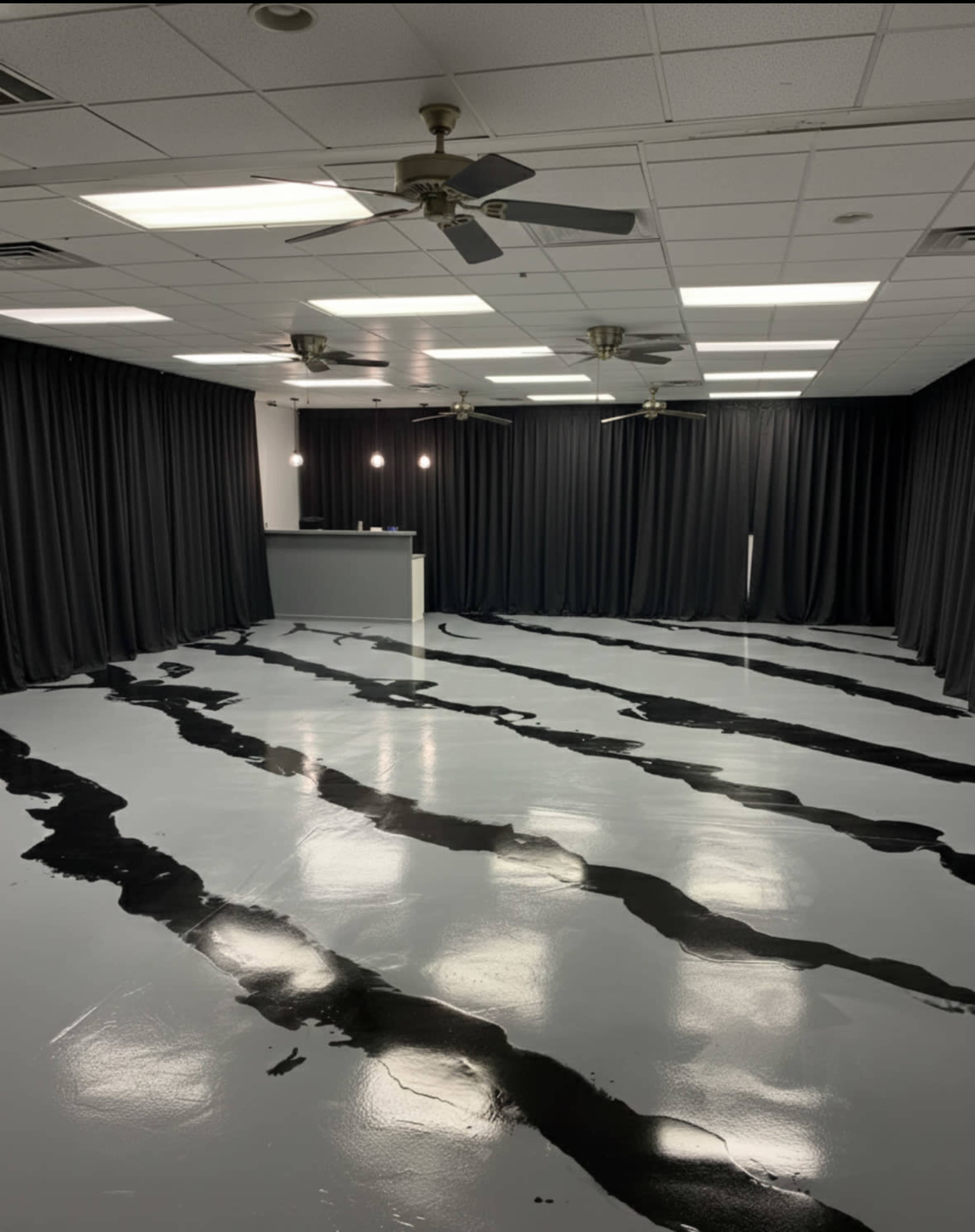 The image shows a spacious, empty room with black and white striped flooring, black curtains along the walls, and several ceiling fans.