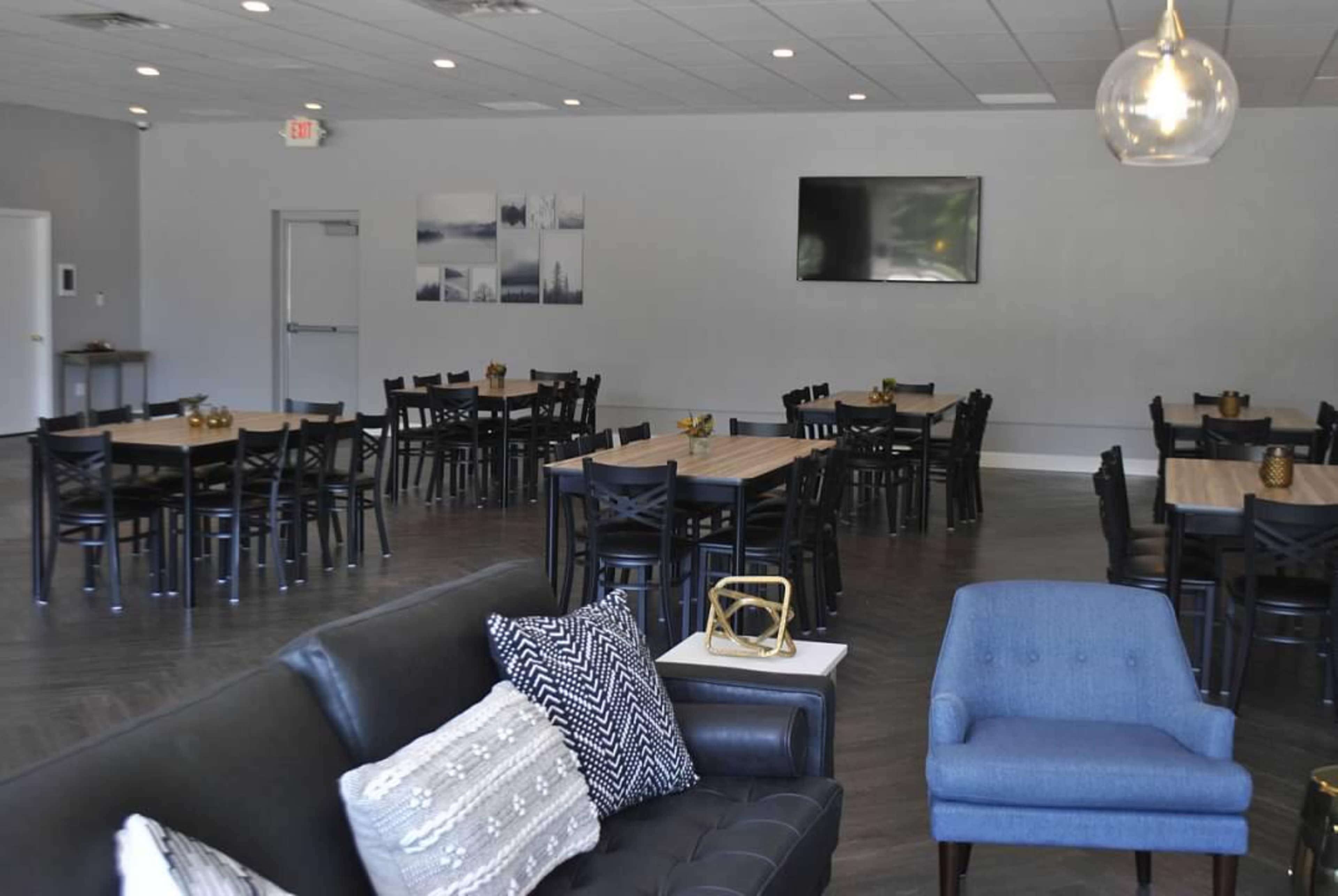 A spacious dining area with multiple tables and chairs, a large television mounted on the wall, and a seating arrangement including a black couch and a blue chair.