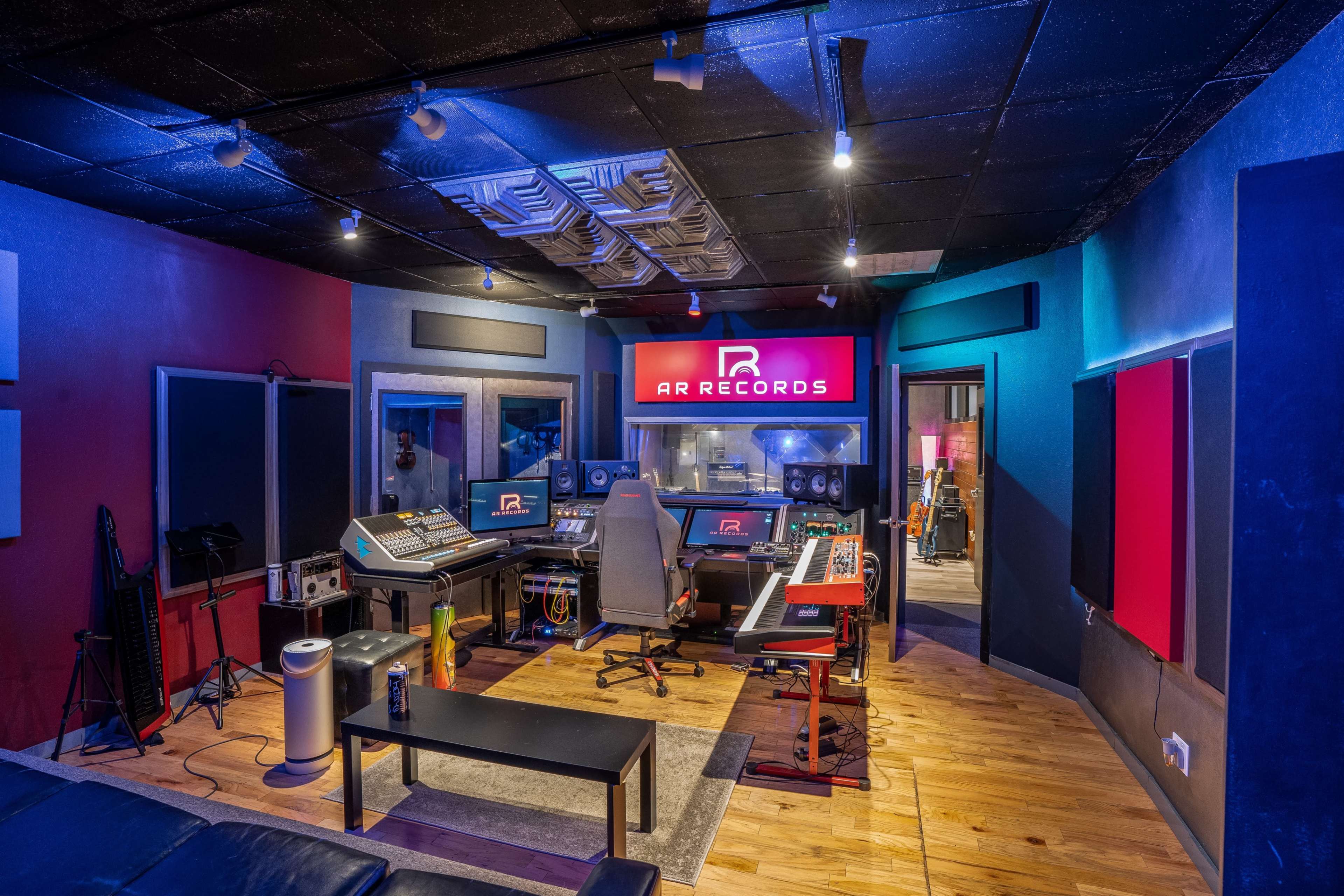 A modern music recording studio with multiple sound mixing consoles, acoustic panels on the walls, and a prominent "AR RECORDS" sign.