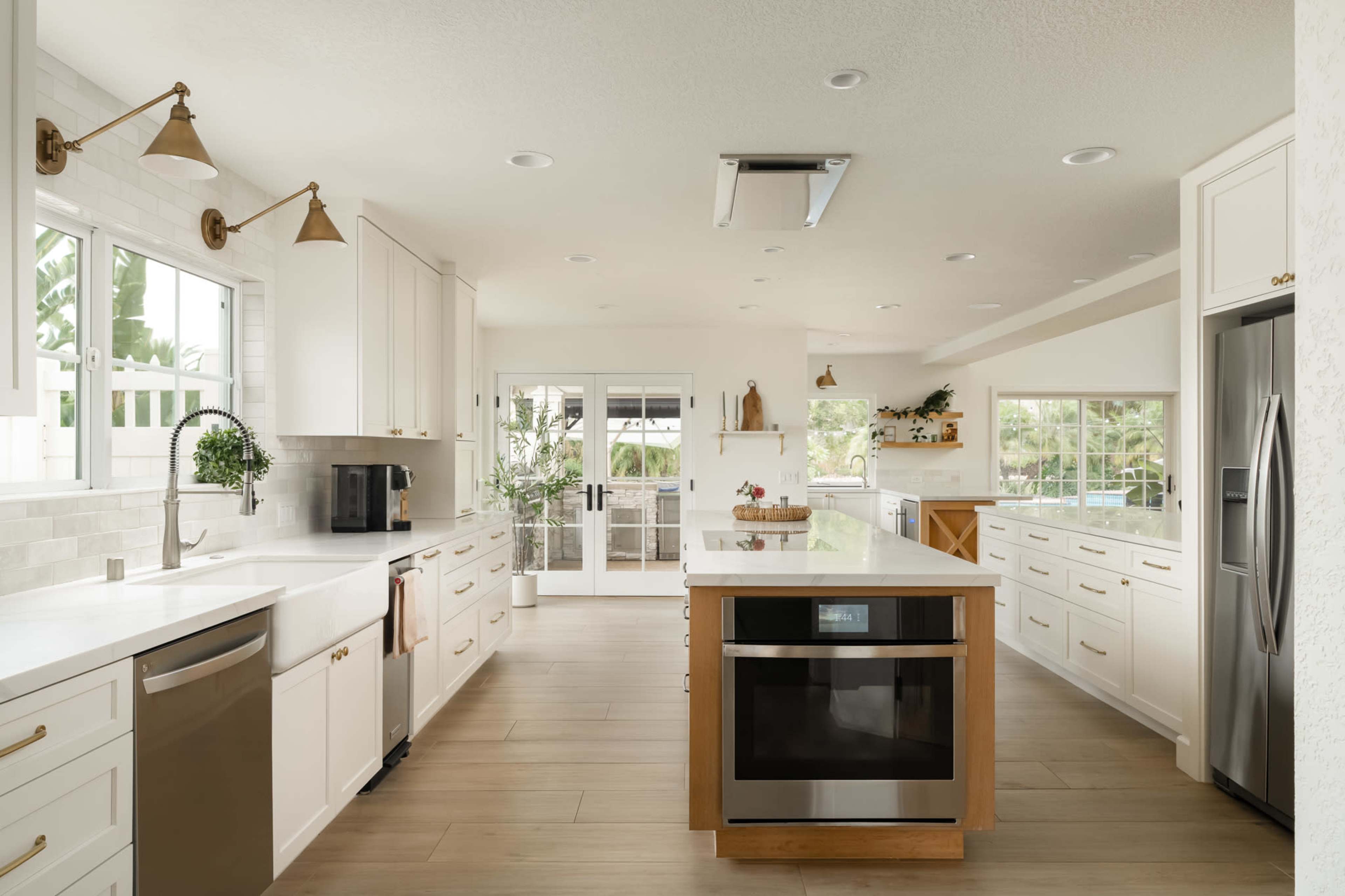 The kitchen features white cabinetry, a large island with an integrated microwave, and stainless steel appliances, with ample natural light coming through multiple windows.