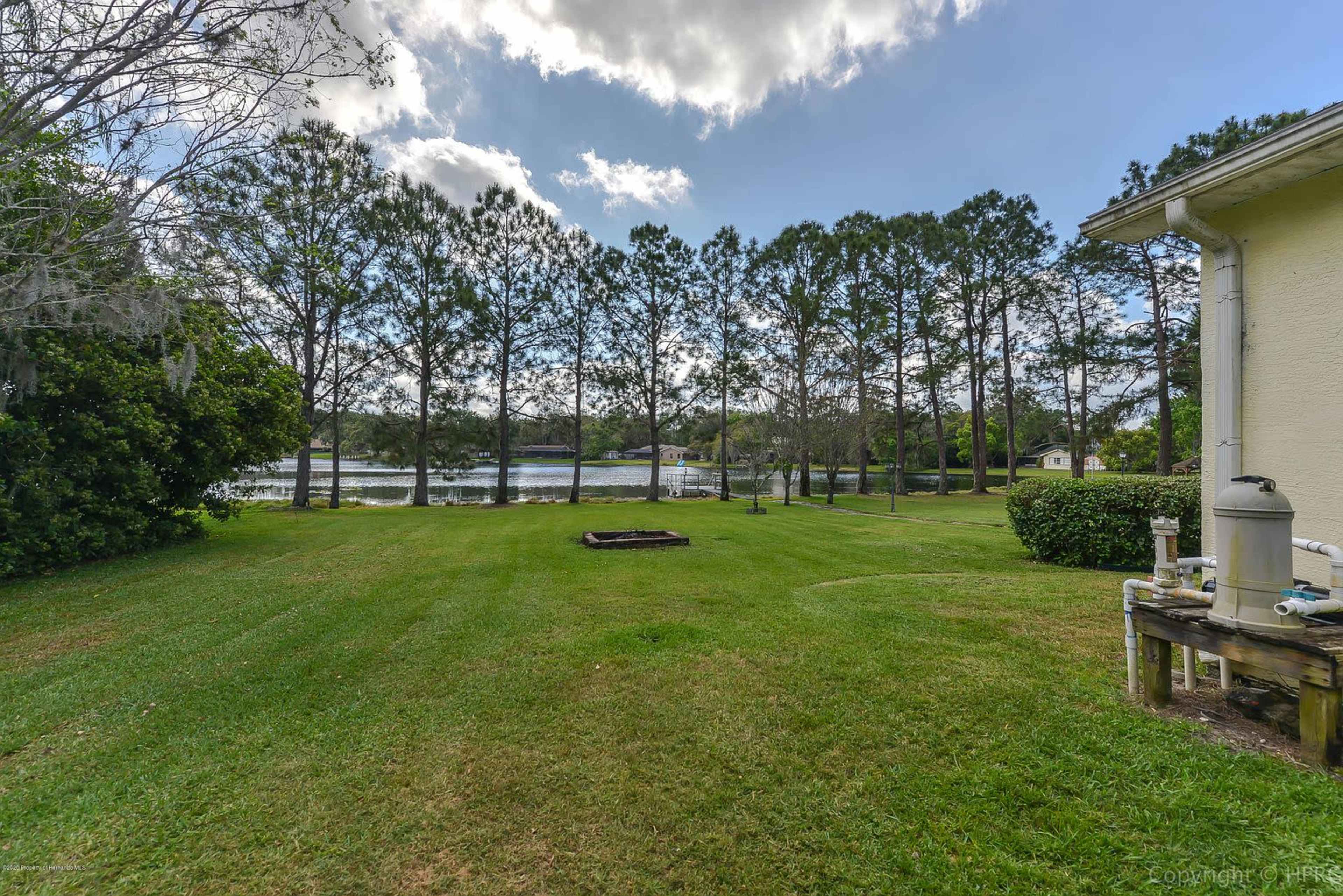 A grassy yard with a view of a lake in the background, bordered by a row of trees on one side.