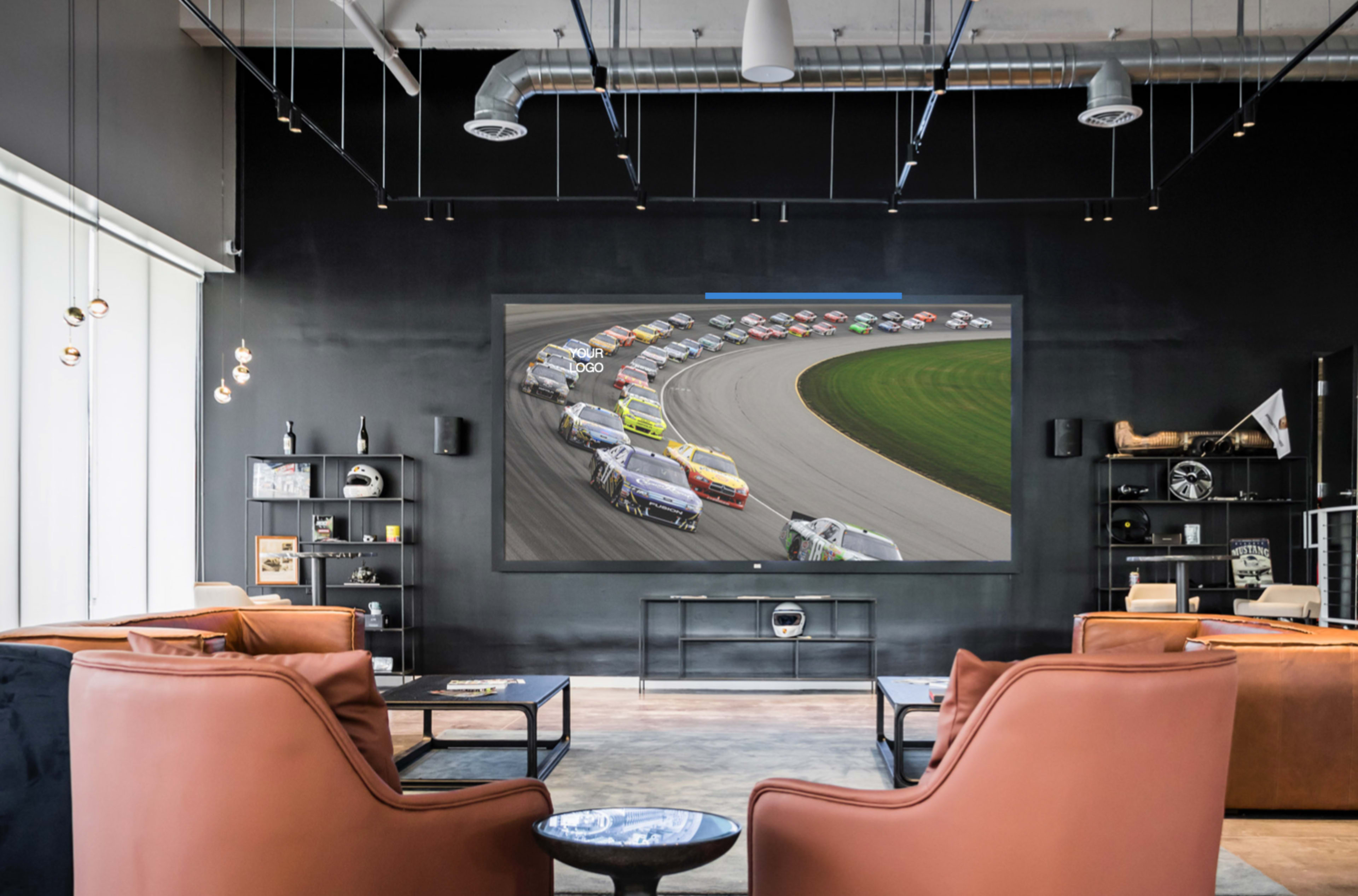 A large screen displays a NASCAR race in a modern lounge area furnished with brown leather chairs and stylish shelves.