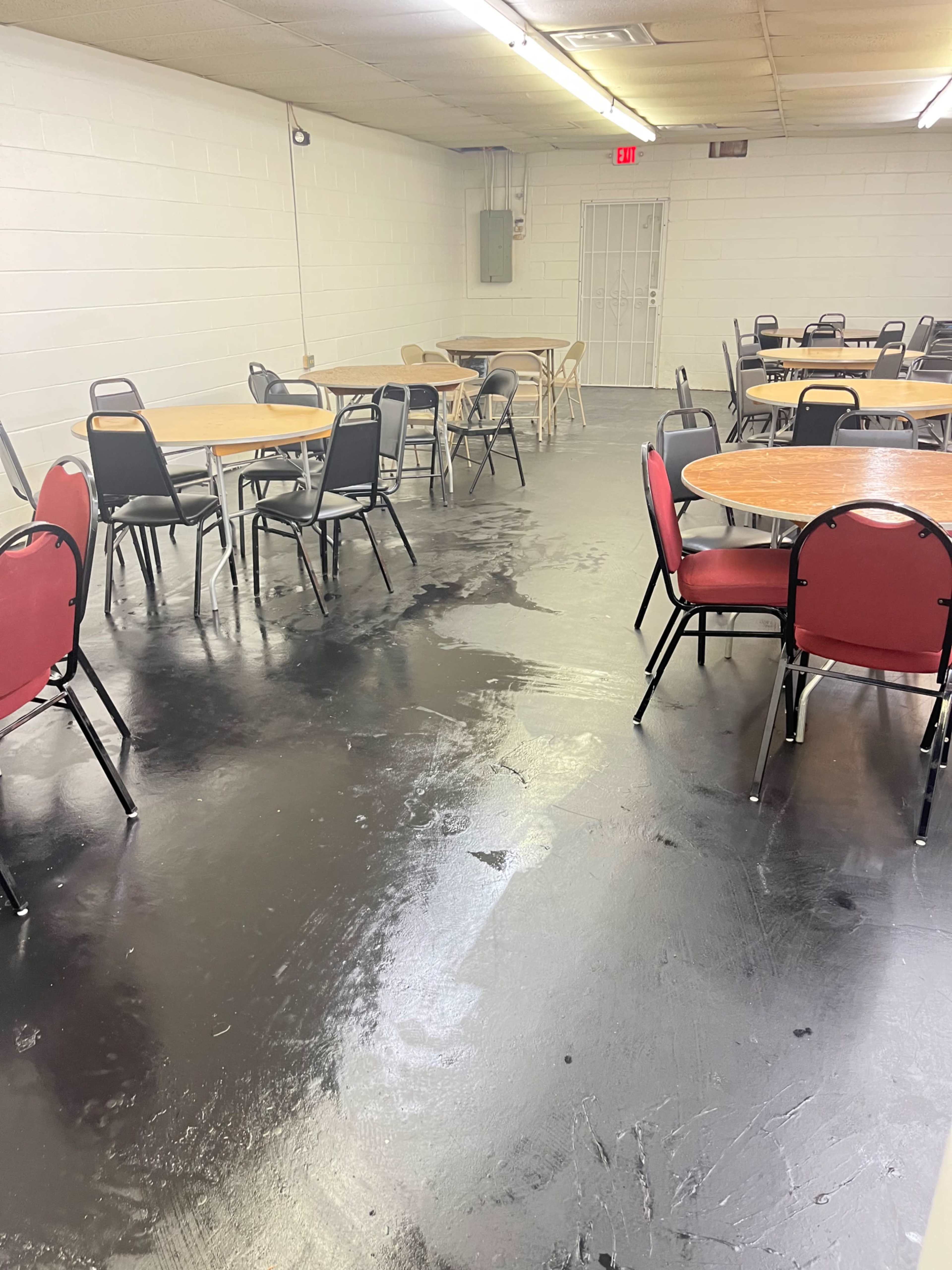 An empty room with several round tables and chairs arranged around a polished black floor.