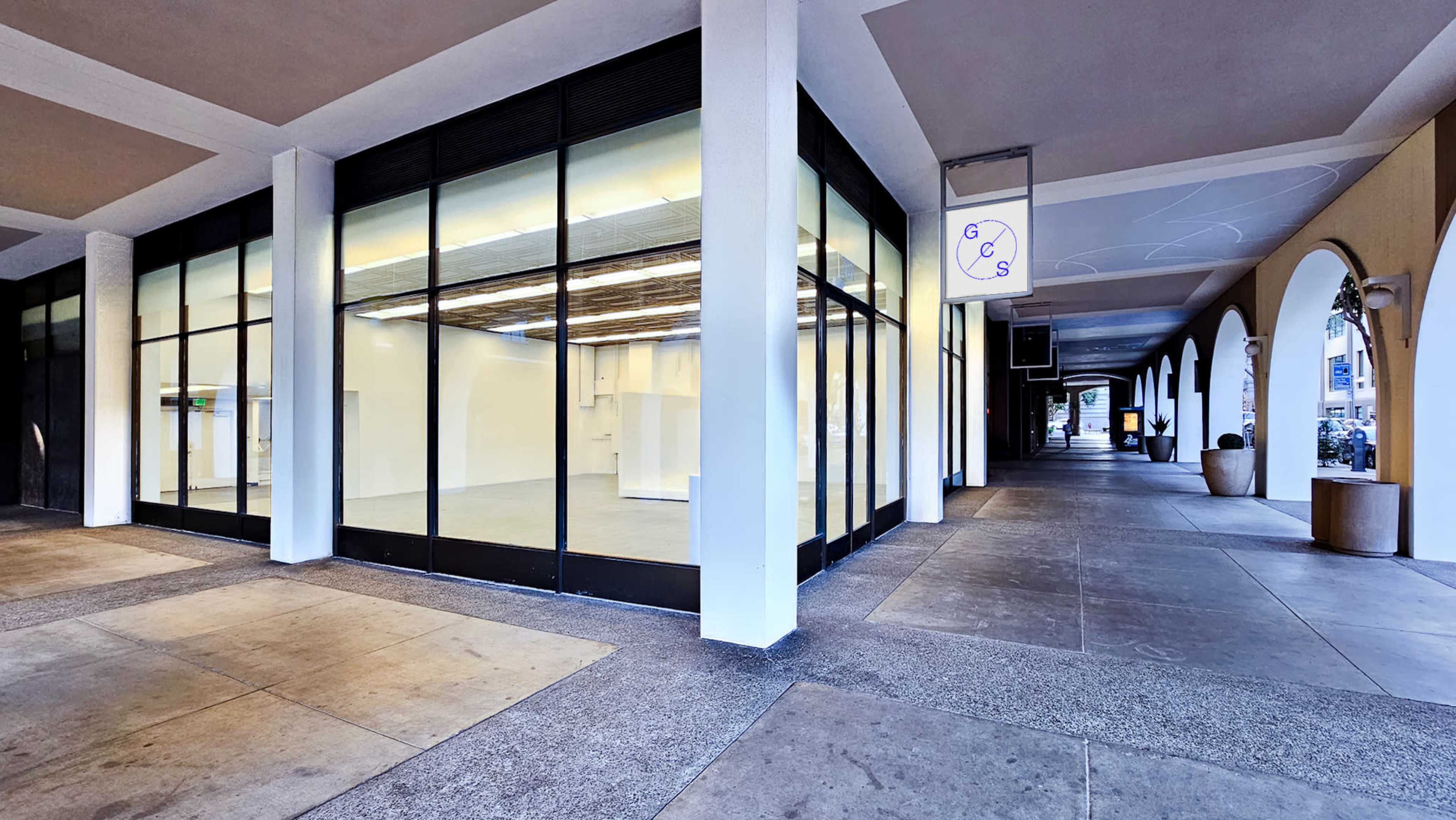 The image shows a modern, empty retail space with large glass windows, situated in a covered walkway lined with arches.