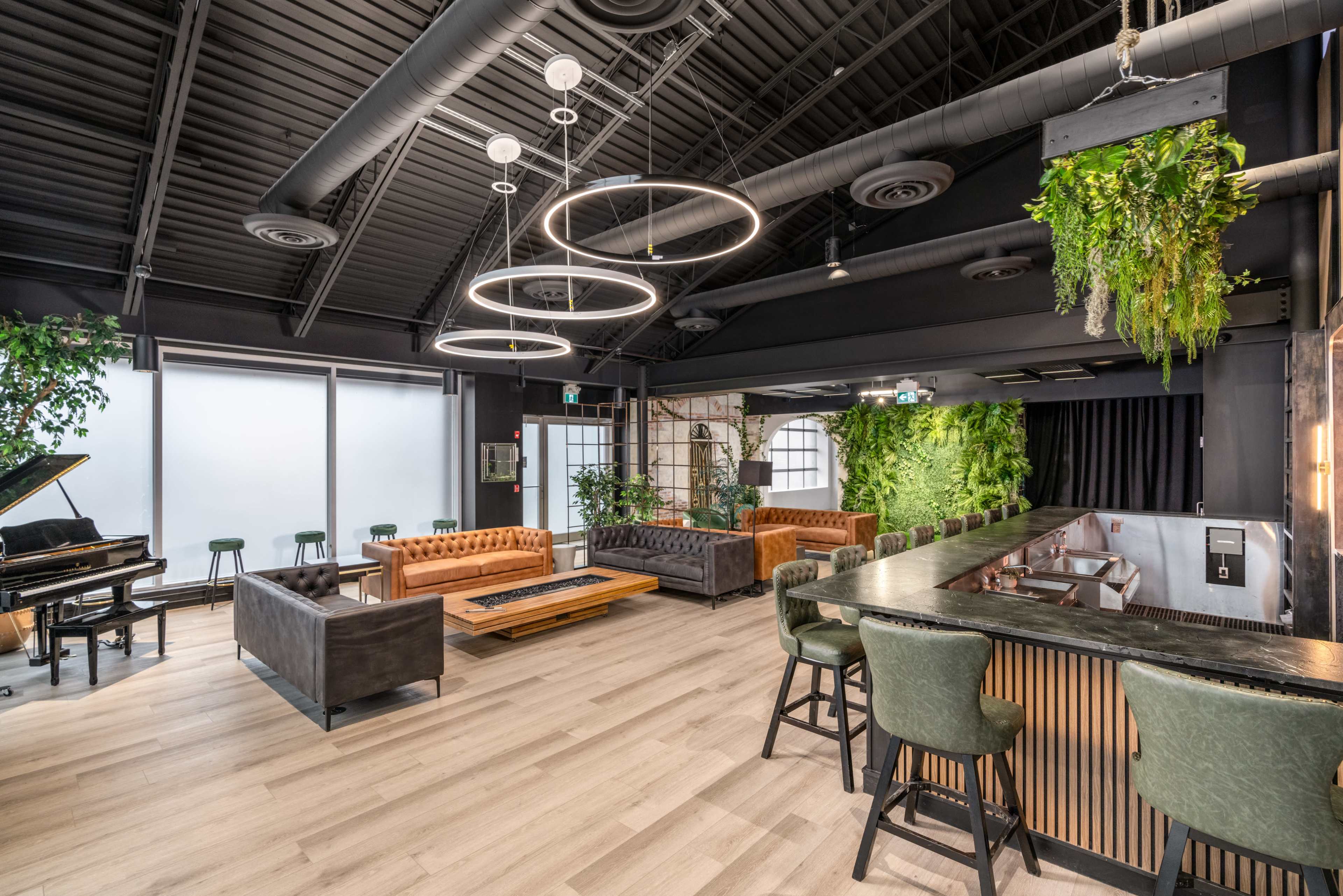 A modern lounge area with leather sofas, a piano, and a bar, featuring plants and unique circular light fixtures.