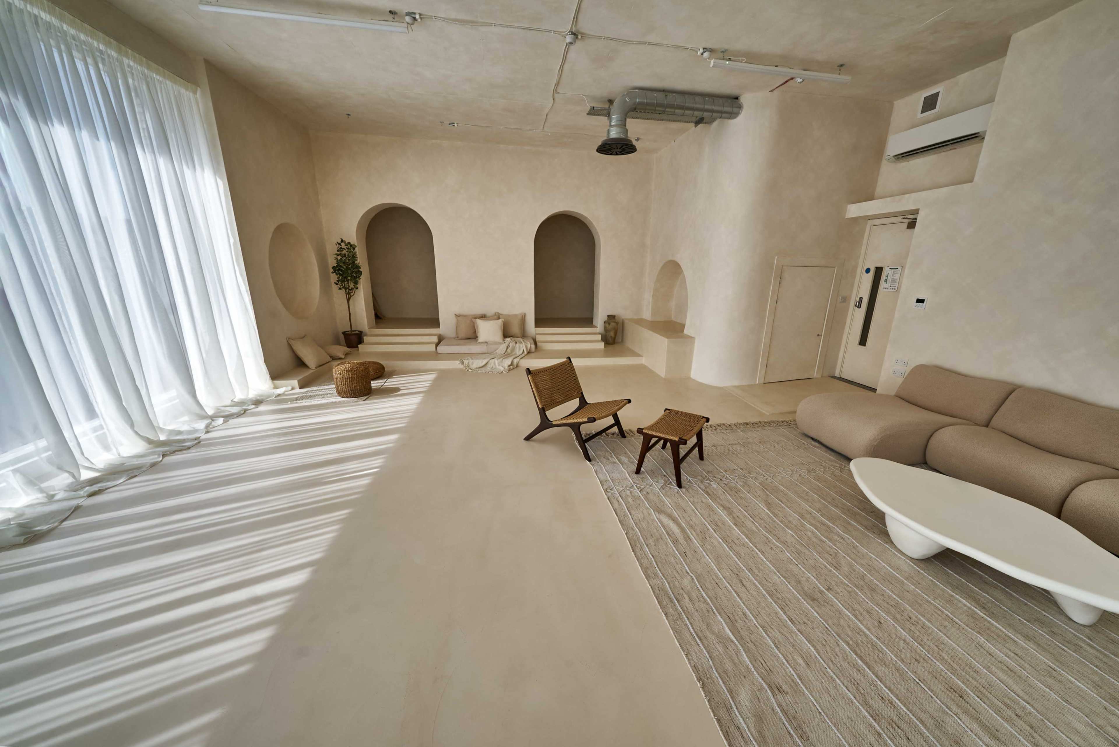 The image shows a spacious, minimalistic interior with arched alcoves, light-colored walls, and simple furniture arranged in an open layout.