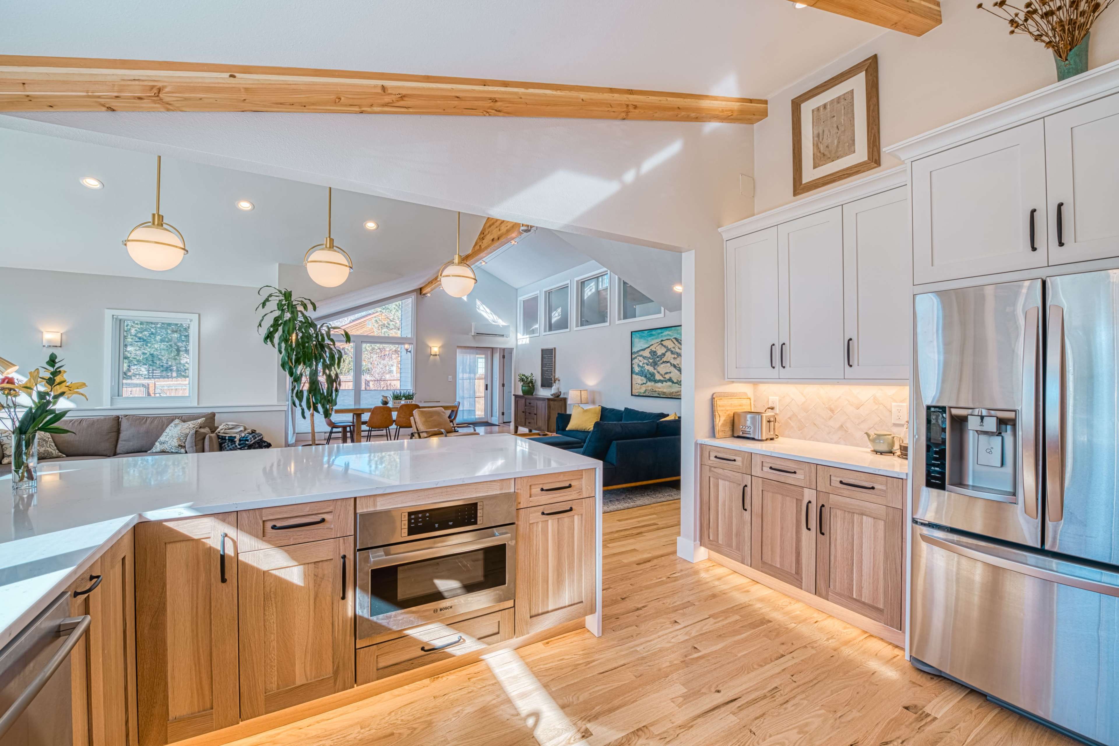 A modern kitchen features a spacious island with a built-in oven, wood cabinetry, and stainless steel appliances, all within an open-concept layout.