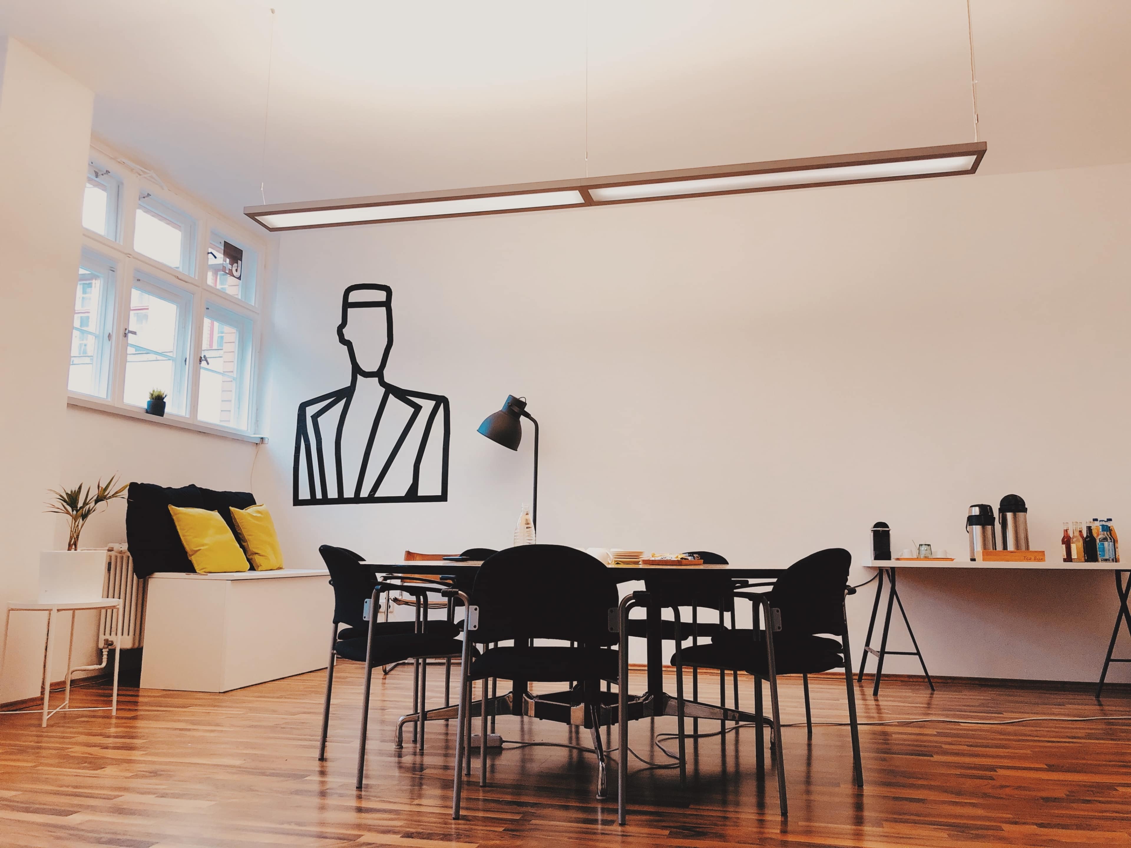 A dining area features a large wall mural of a person, a table with black chairs, and a sideboard displaying drinks and snacks.