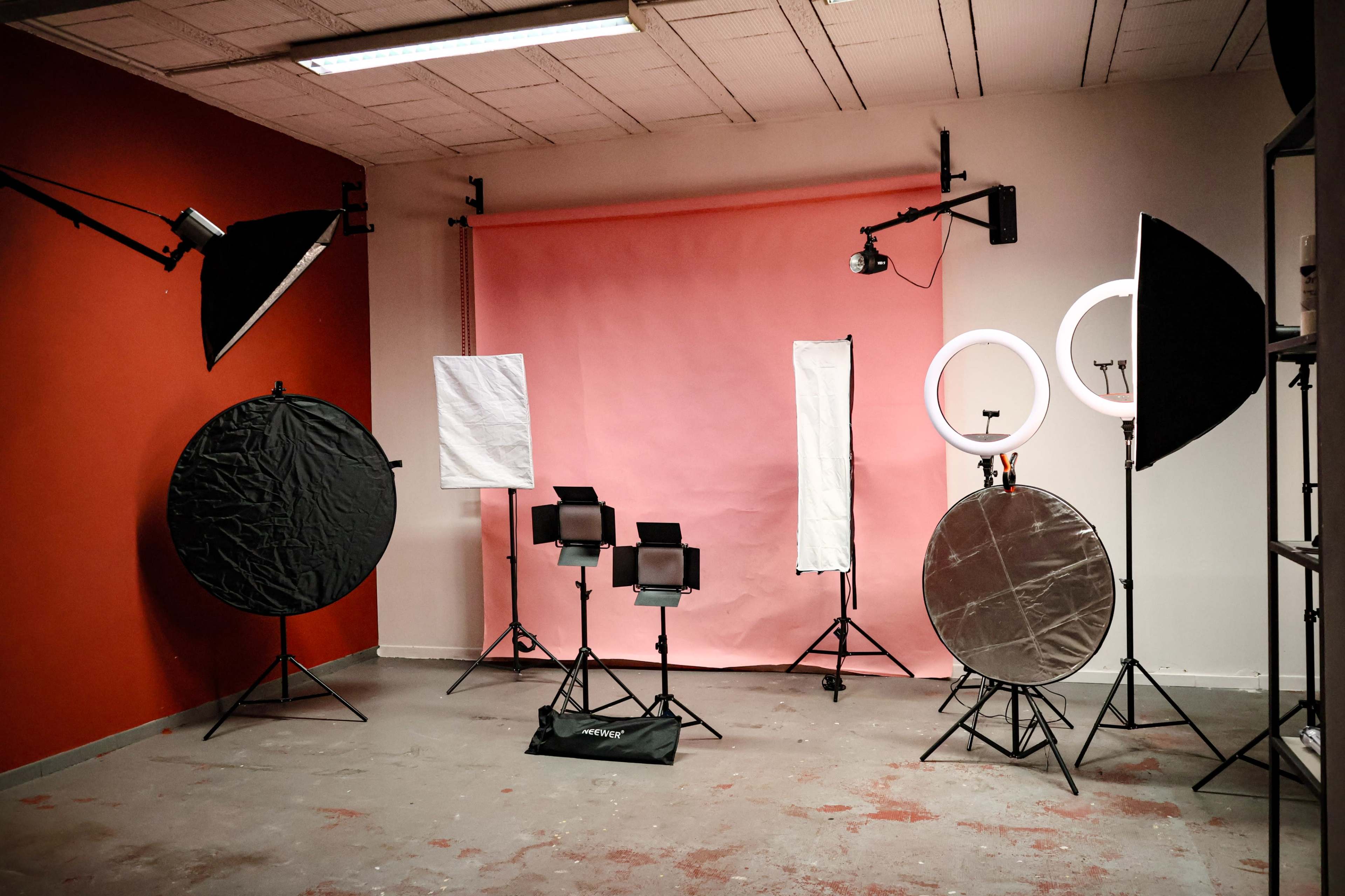 The image shows a photography studio setup with various lighting equipment and a pink backdrop.