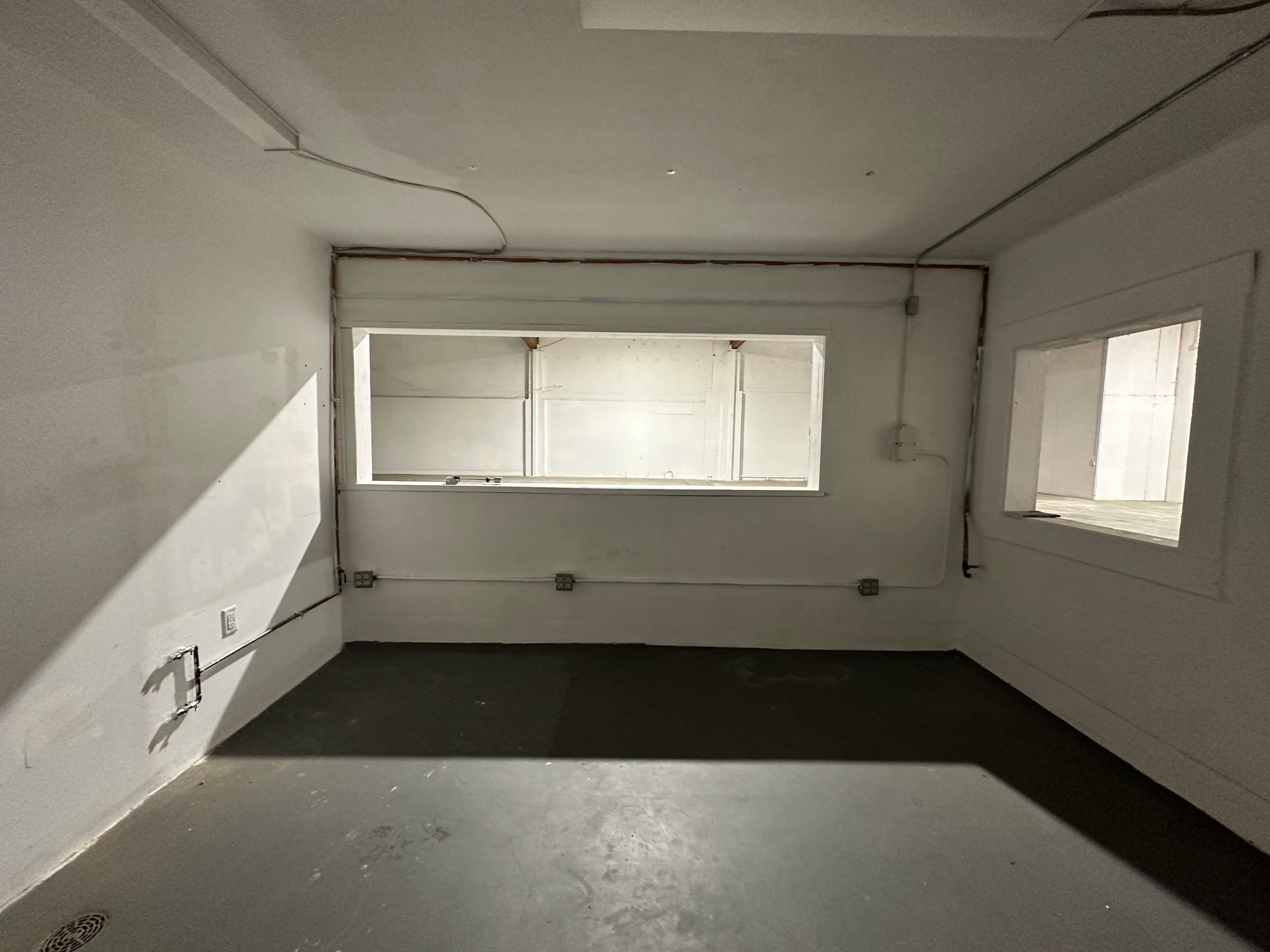 An empty room with white walls, a gray floor, and two windows allowing light to enter.