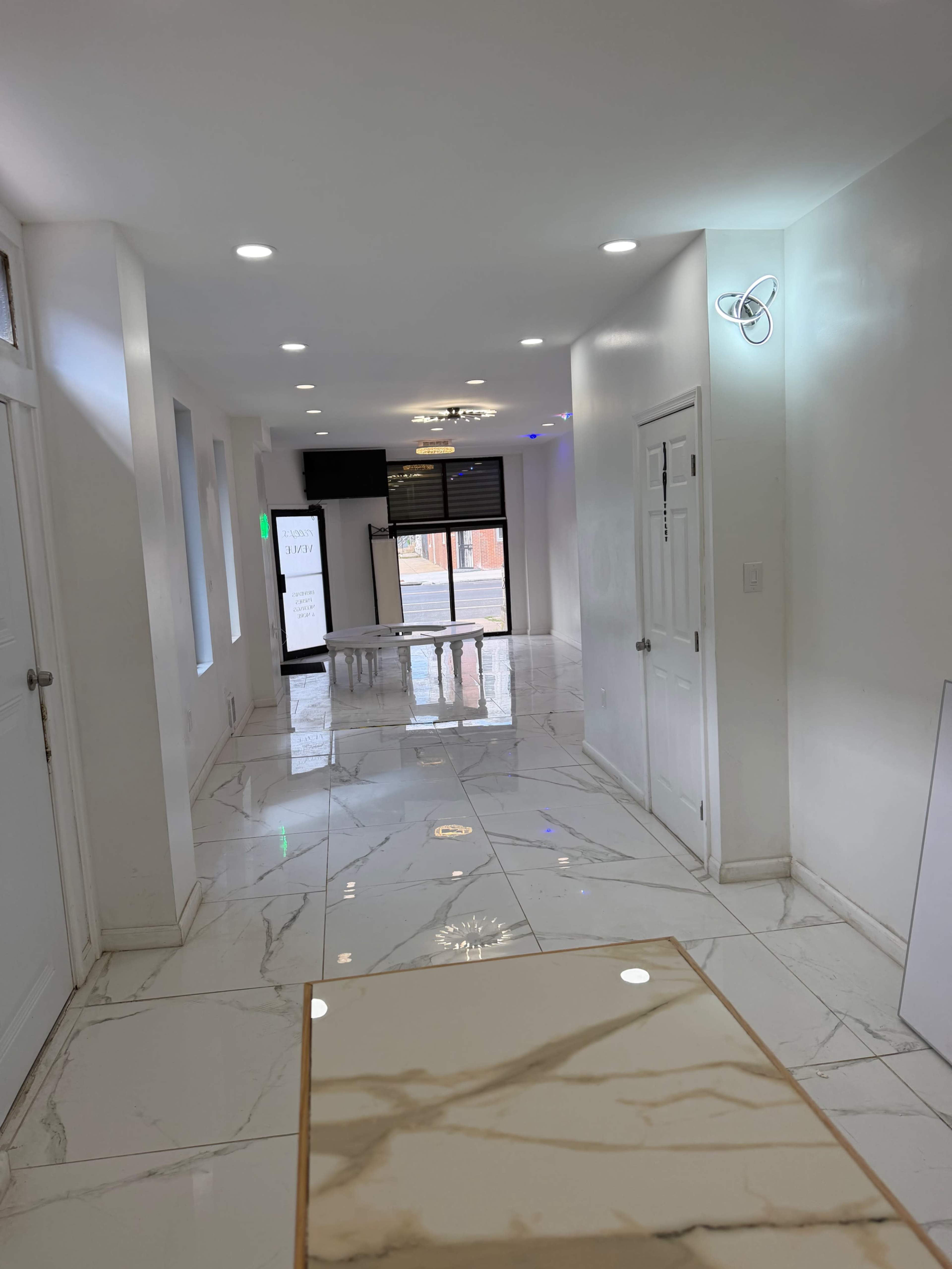 The image shows a bright, modern hallway with glossy white tiles and several doors along the sides.