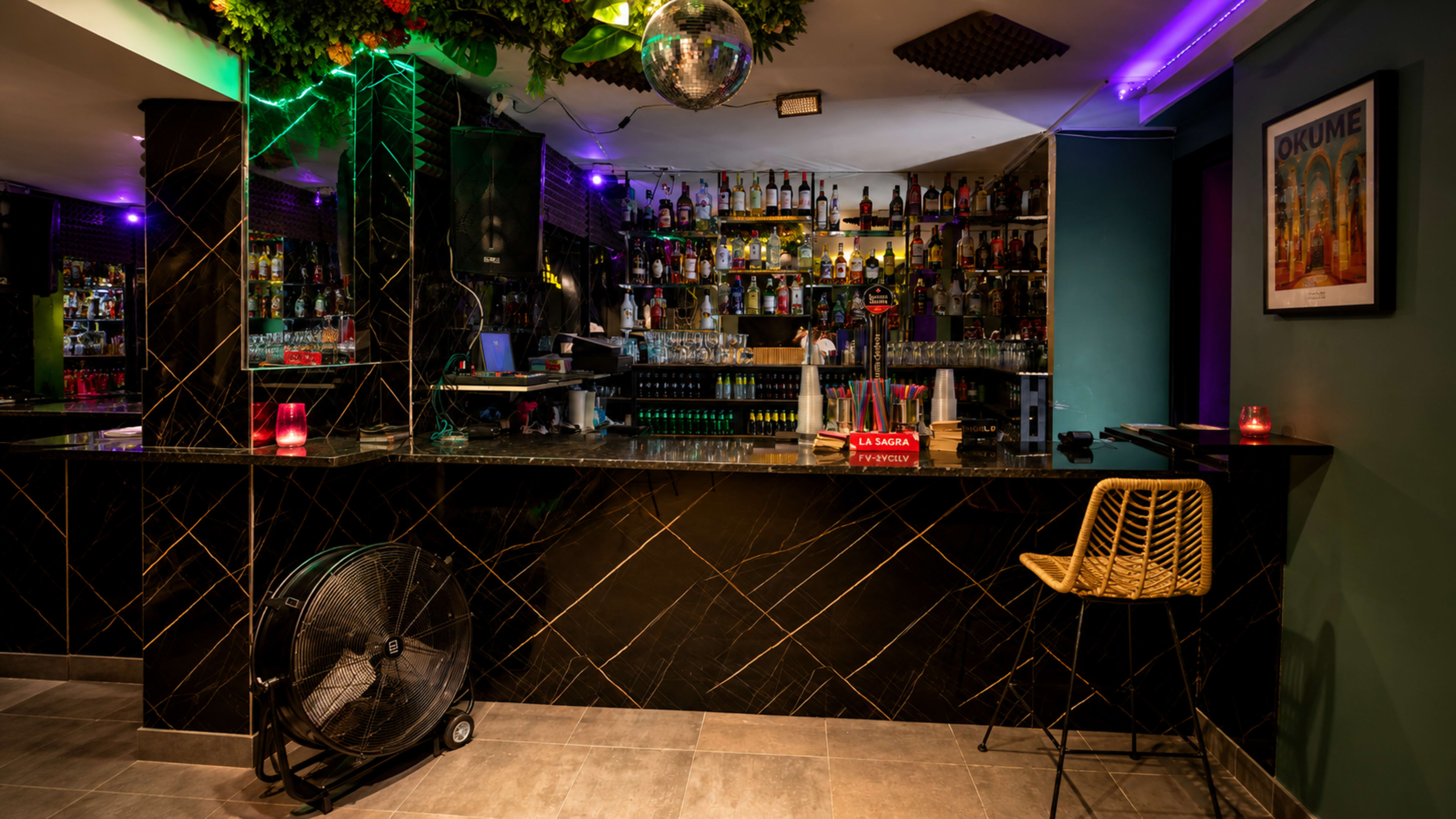 The image shows a bar area with a black marble counter, shelves filled with various bottles, and colorful lighting, including a disco ball hanging from the ceiling.