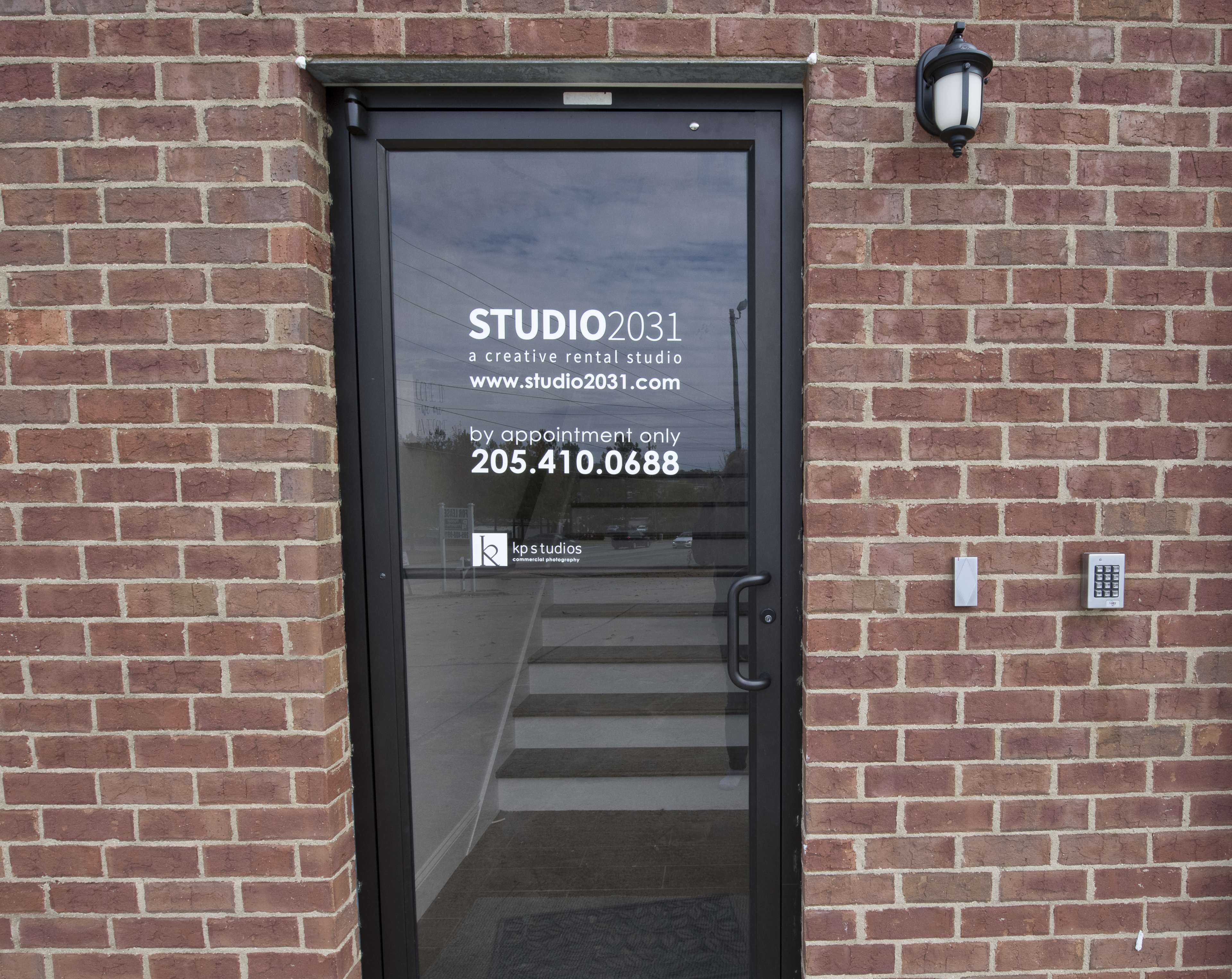 The image shows a dark glass door with a sign indicating it is Studio 2031, a creative rental studio, along with contact information and instructions for appointments.