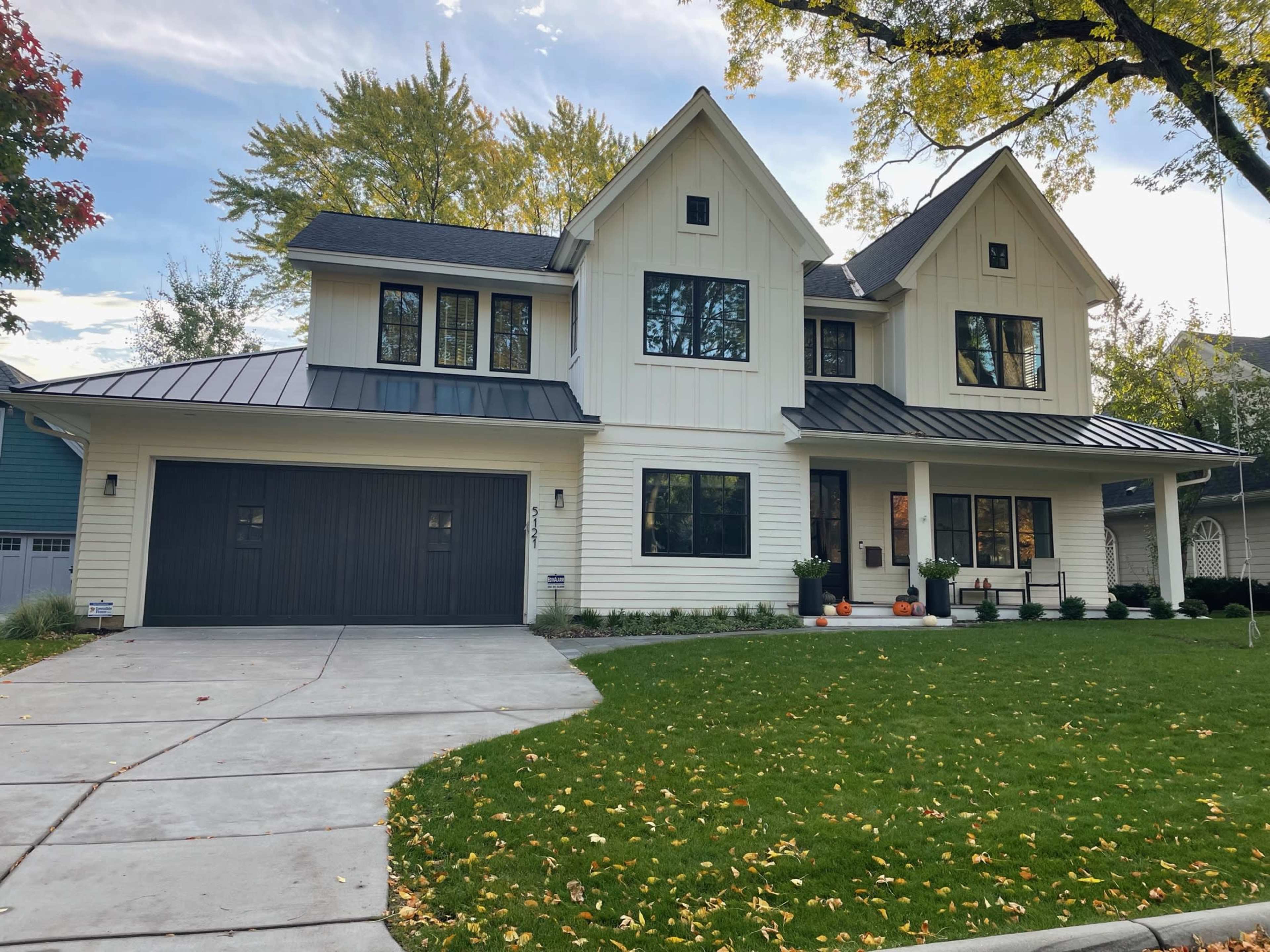 A modern two-story house with a white exterior, a black metal roof, and a neatly landscaped front yard.