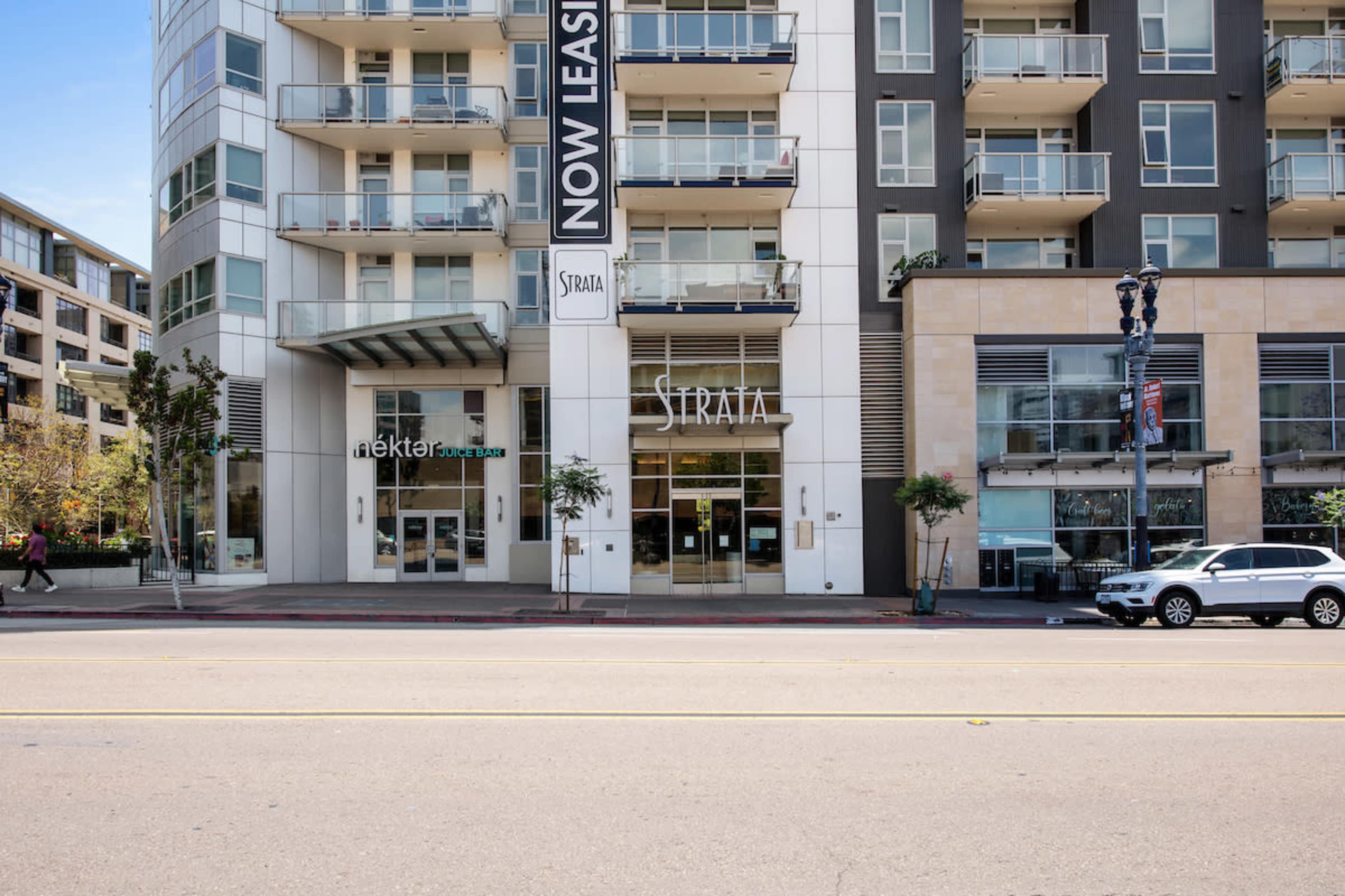 A modern apartment building with a "Now Leasing" banner and a storefront labeled "Strata."