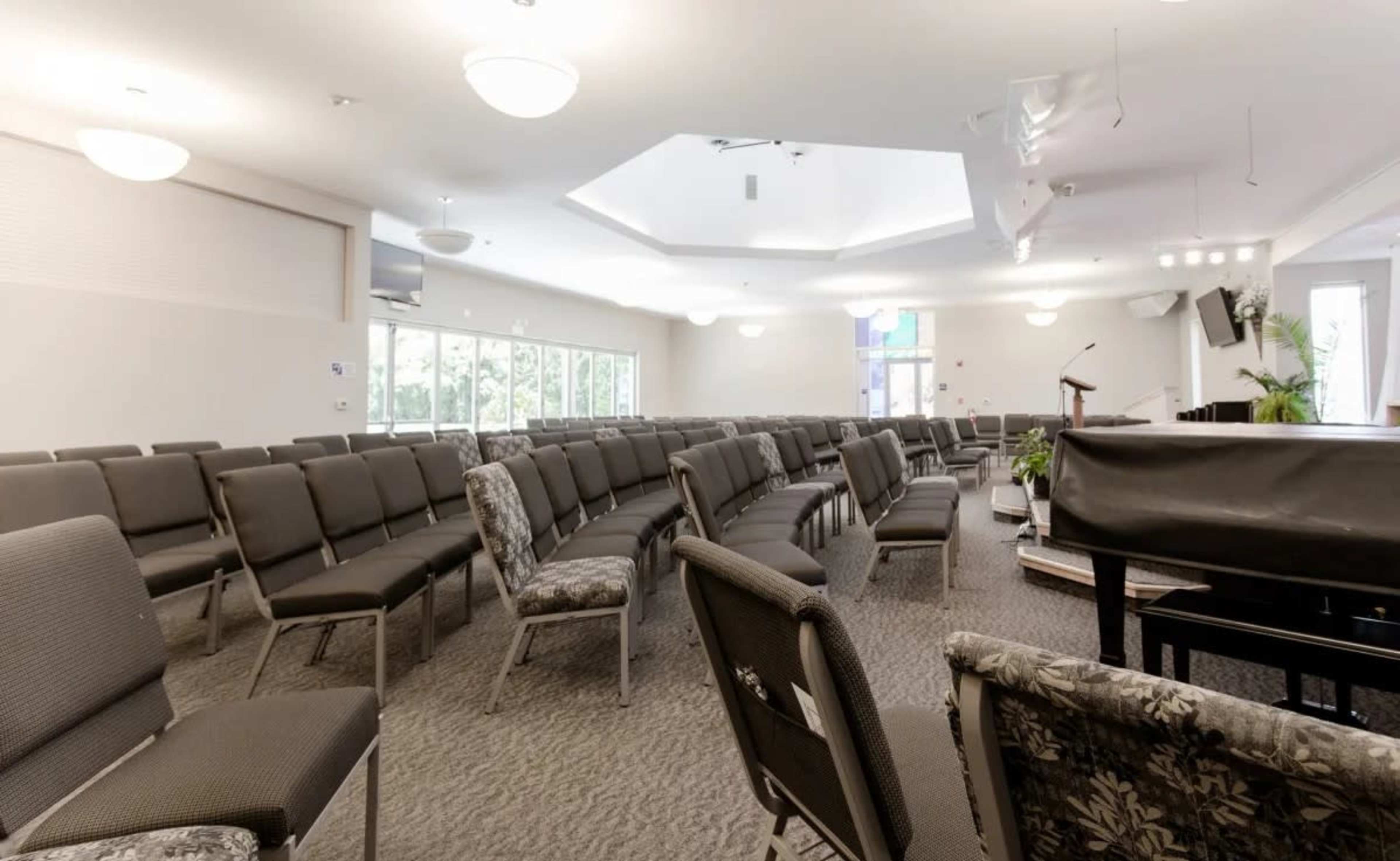 A spacious room arranged with rows of chairs facing a stage that includes a piano and a podium.