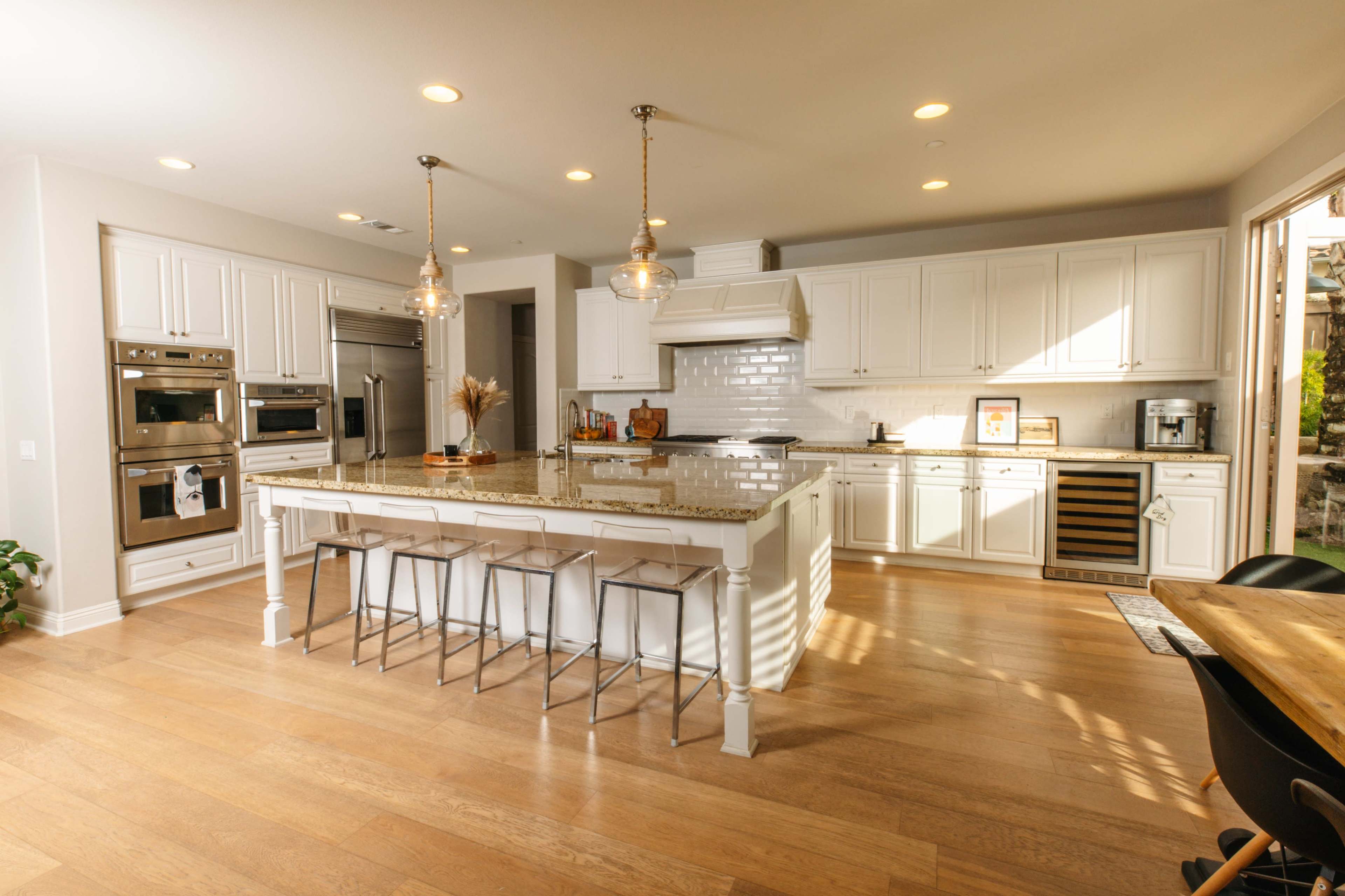 A modern kitchen features white cabinetry, stainless steel appliances, a large island with seating, and ample natural light.