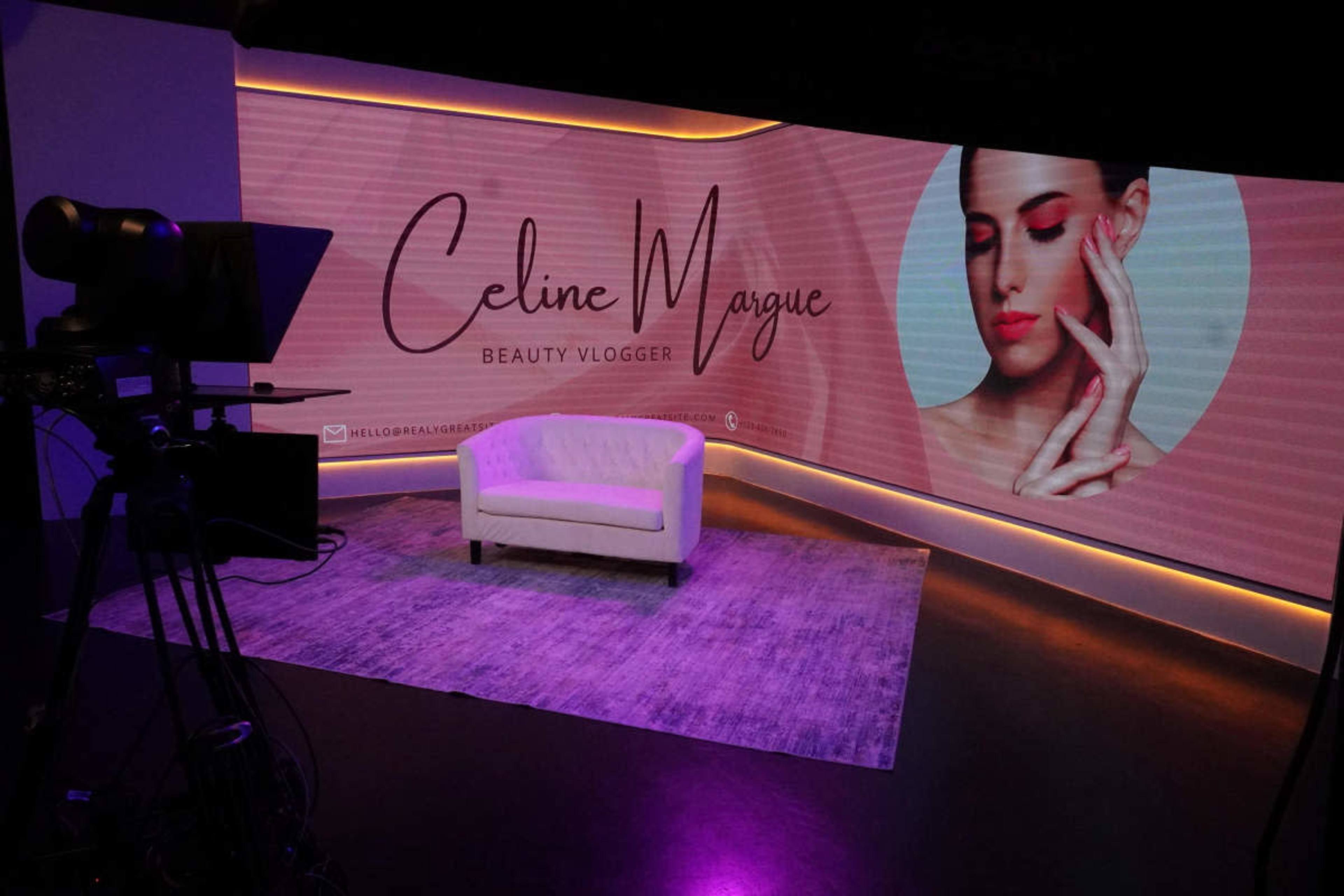 A brightly lit TV studio features a white couch and a large backdrop displaying the name "Celine Wague" alongside a beauty vlogger theme.