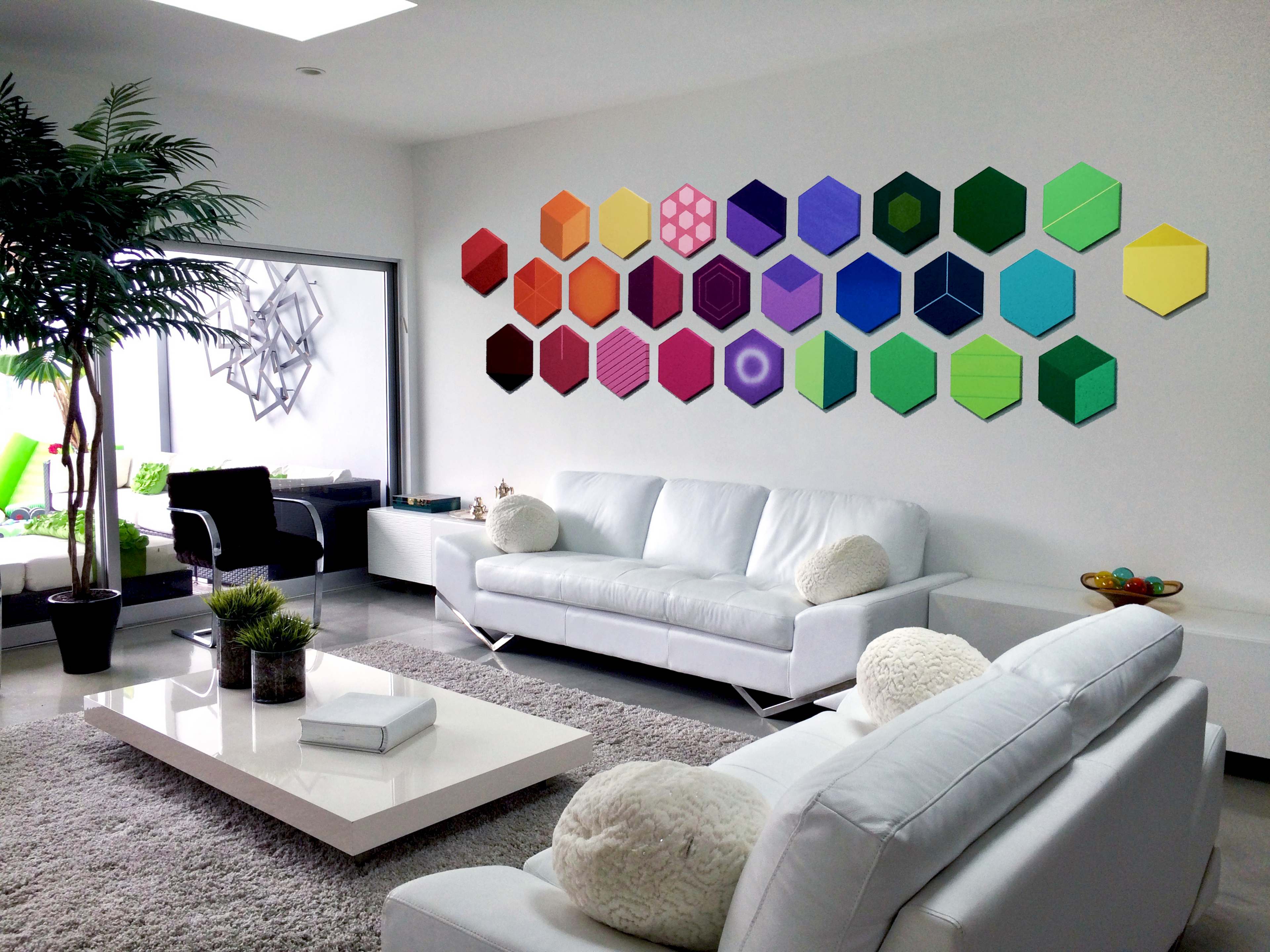 A modern living room features two white sofas facing a hexagonal-patterned wall art display in various colors, with a coffee table and a decorative plant in the foreground.