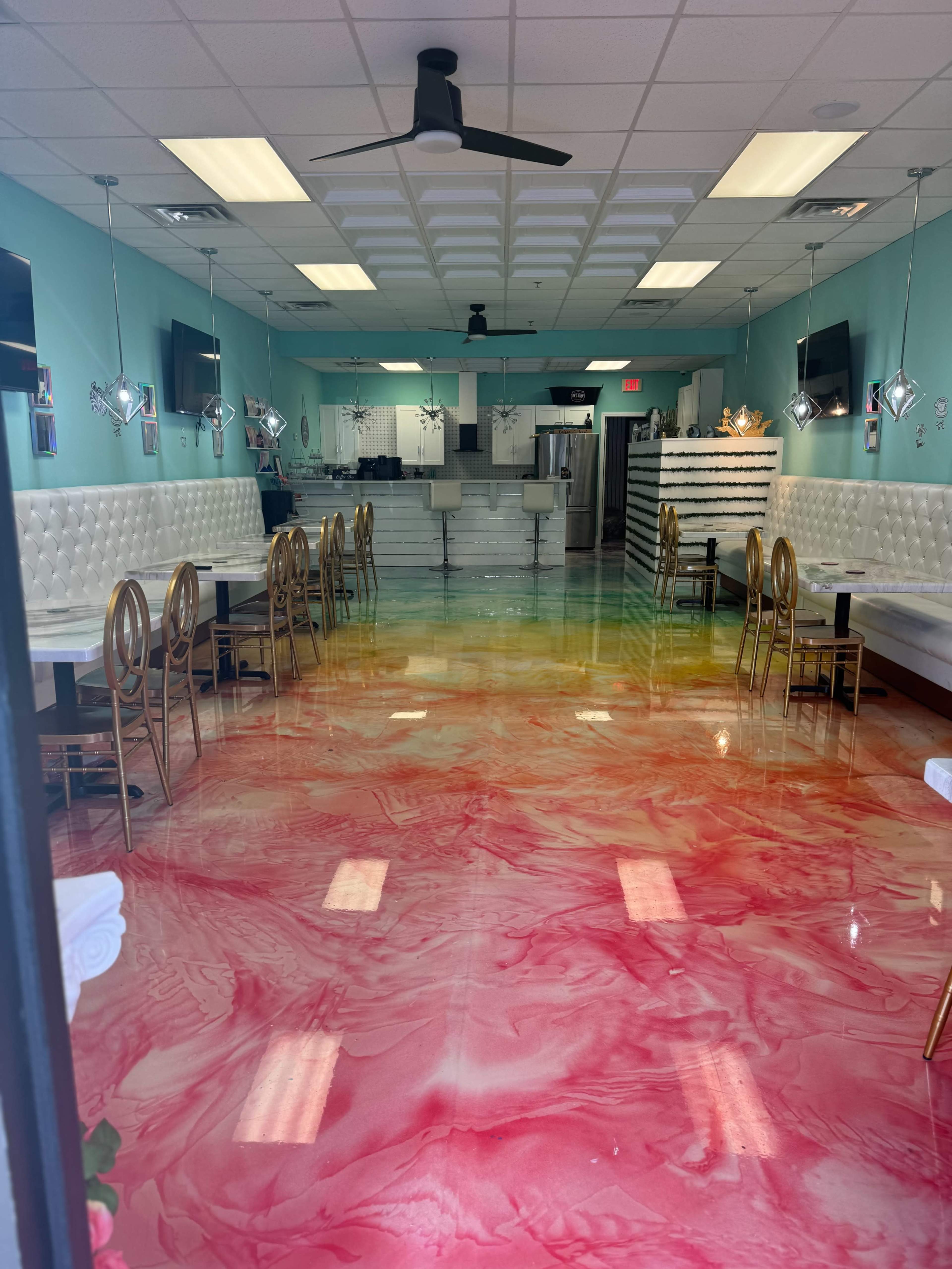 A colorful interior of a dessert shop, featuring a marbled pink and yellow floor, white leather seating, and modern decor with wall-mounted televisions.
