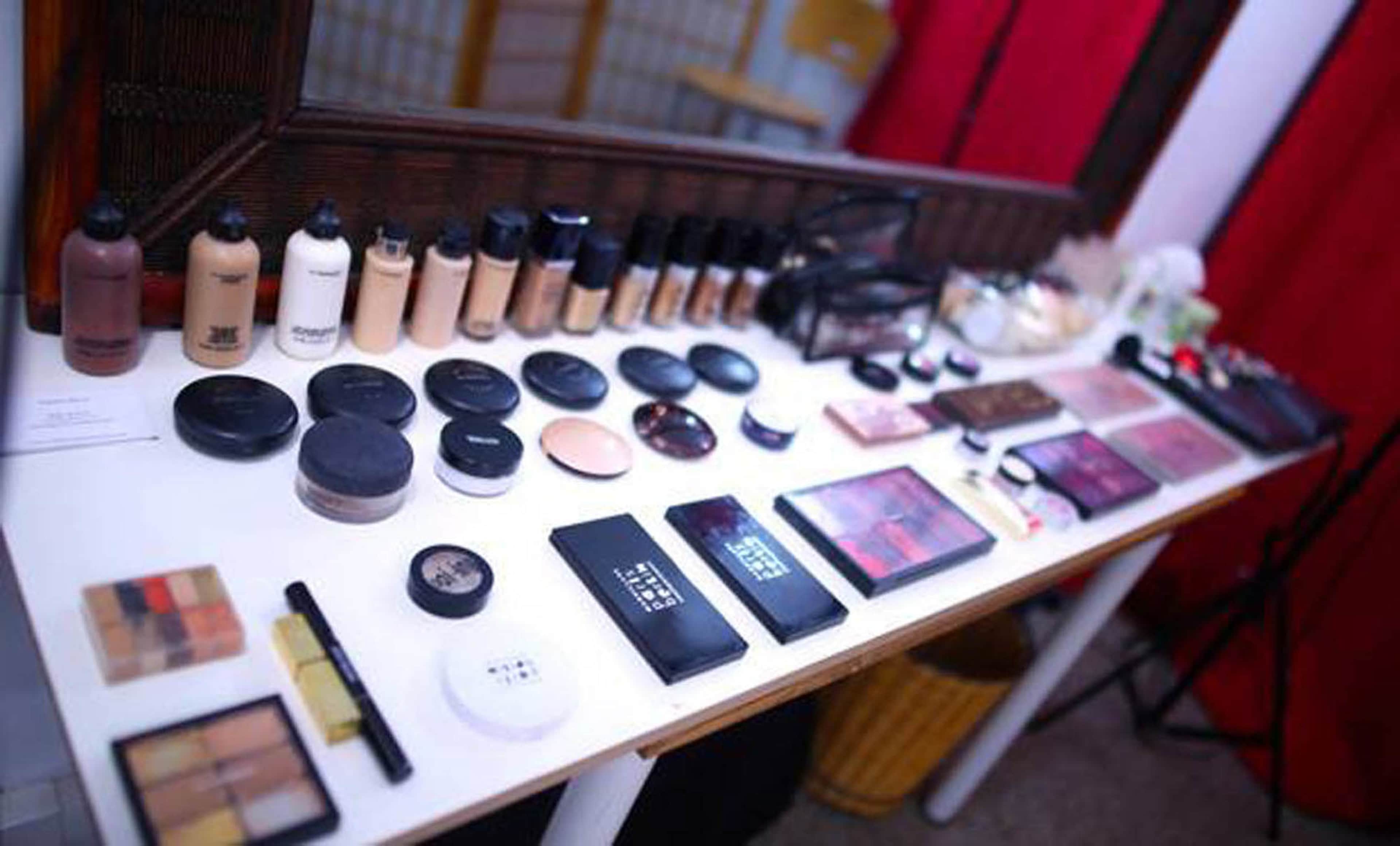 A table displays a variety of makeup products, including foundations, powders, and palettes, organized neatly in front of a mirror.