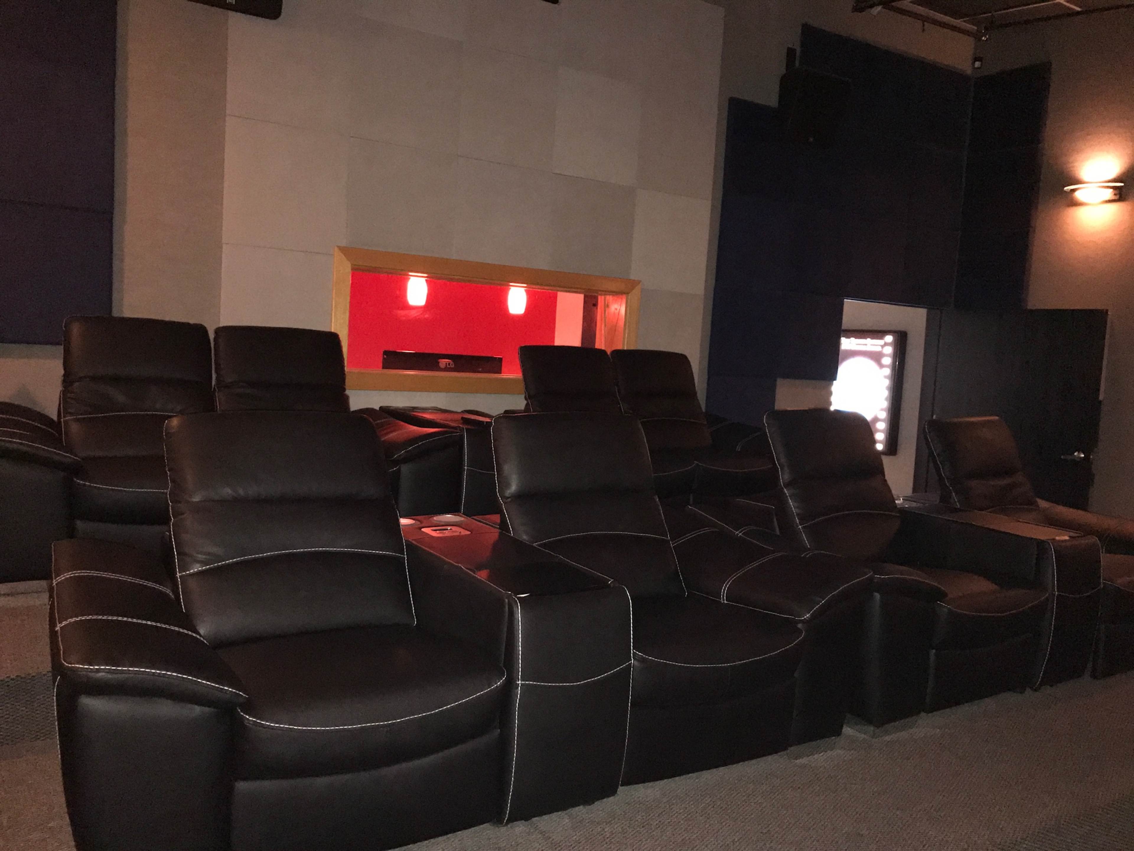 A row of black reclining chairs arranged in a home theater setting with a red-lit area in the background.