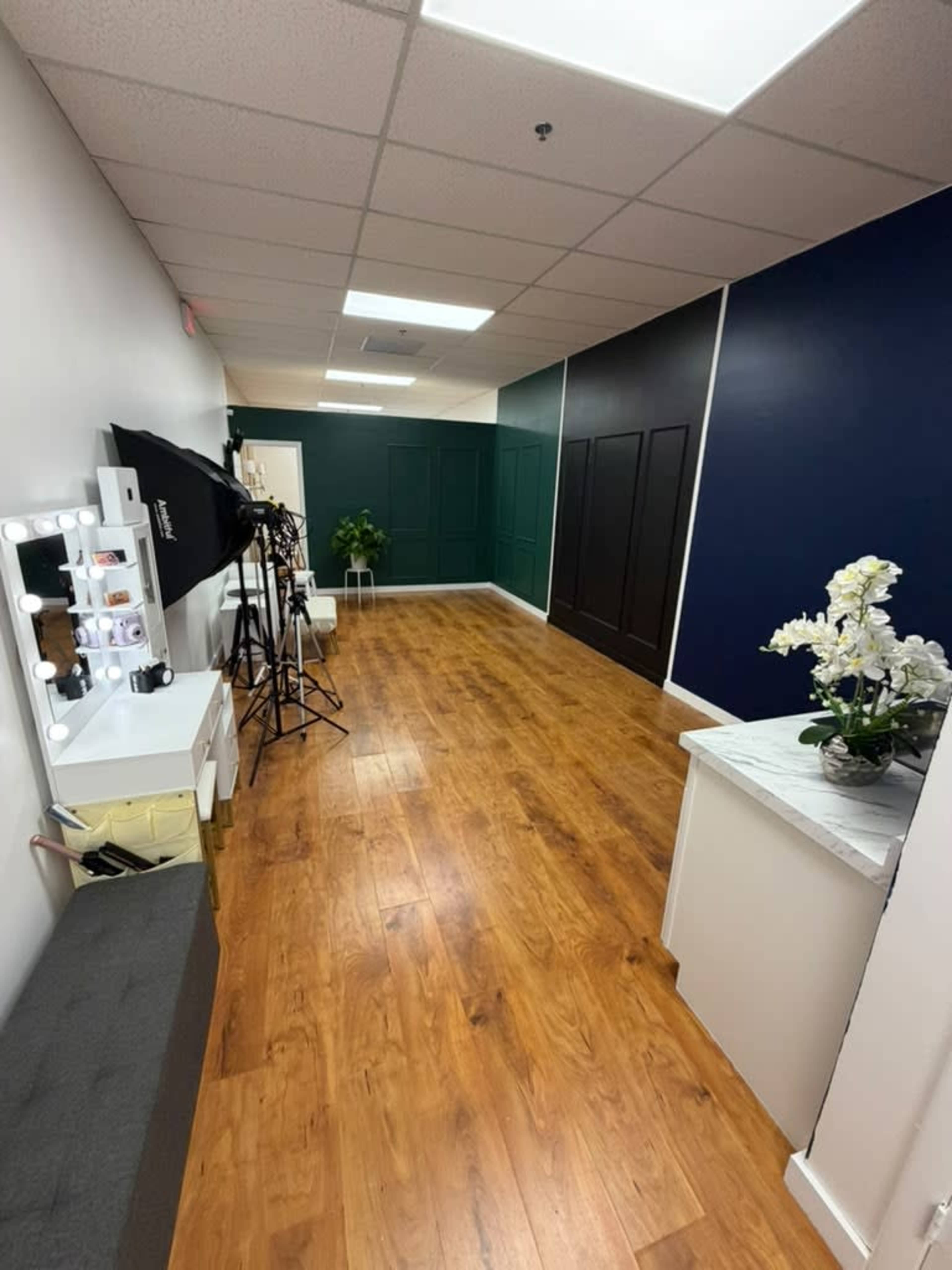 The image shows a well-lit hallway with wooden flooring, green and black accent walls, and photography equipment set up on the left side.