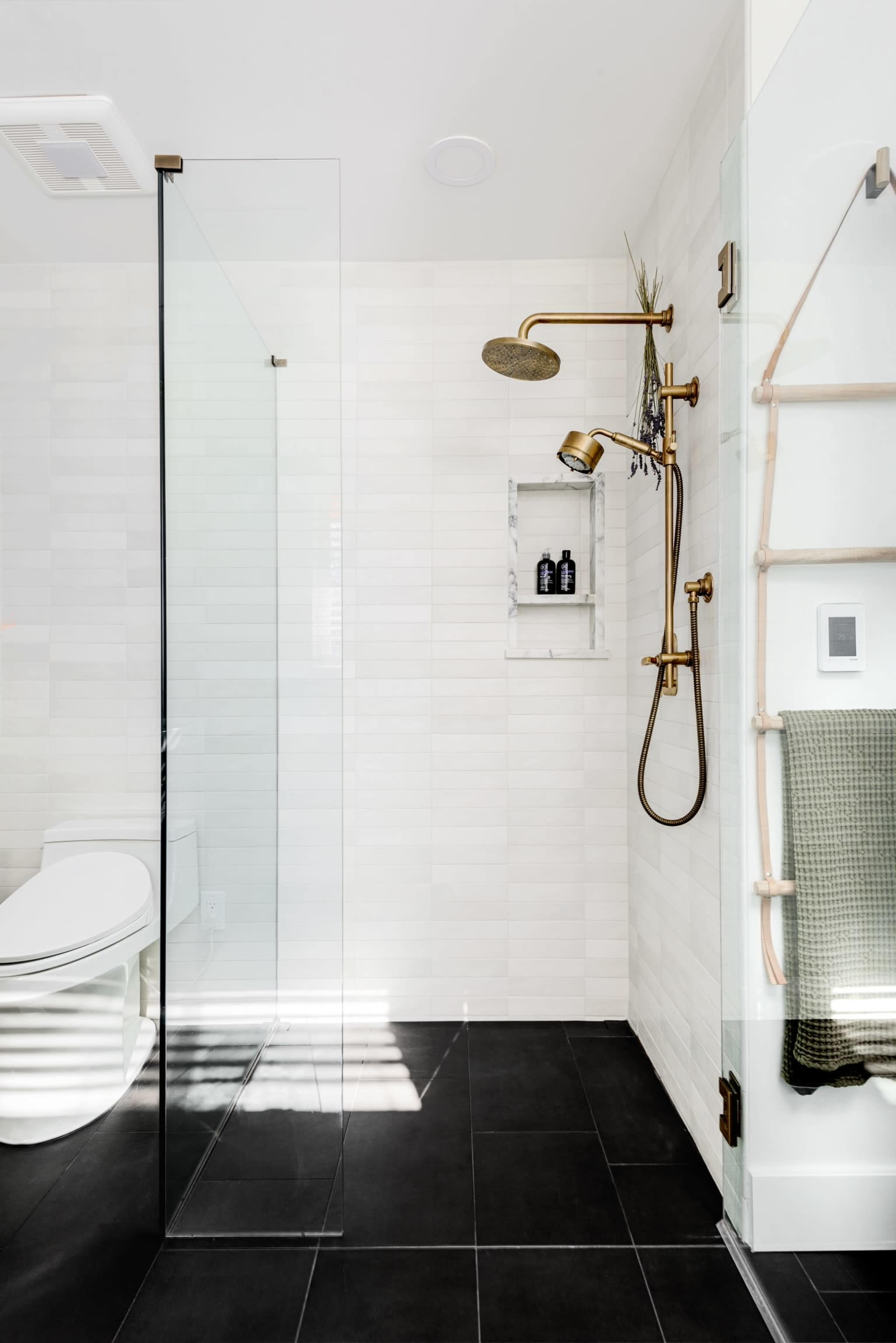 A modern bathroom with a glass shower enclosure, a wall-mounted brass showerhead, and a sleek toilet beside a towel rack.