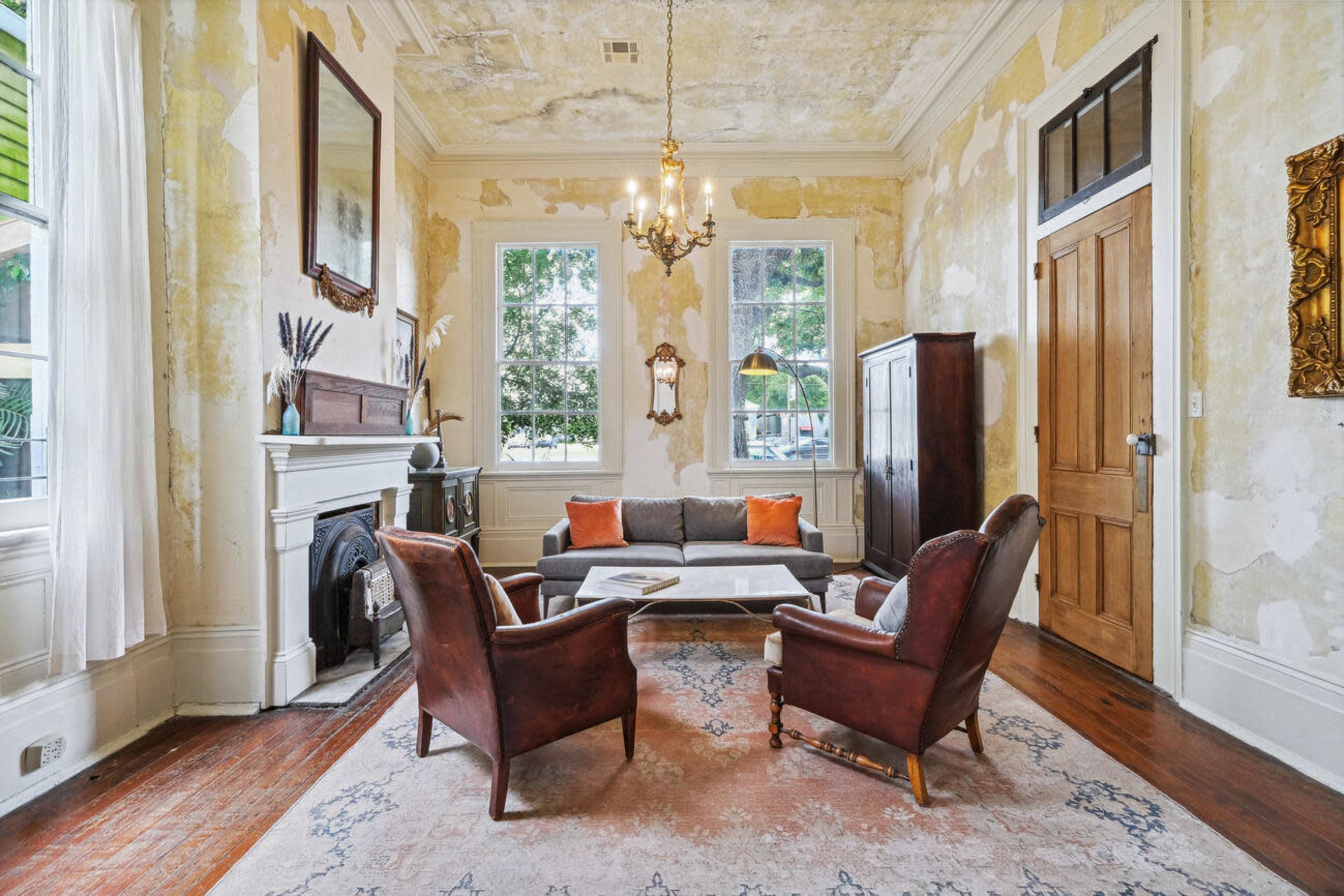 The room features a vintage-style living area with a sofa, two leather armchairs, and a coffee table, surrounded by peeling wallpaper and large windows.