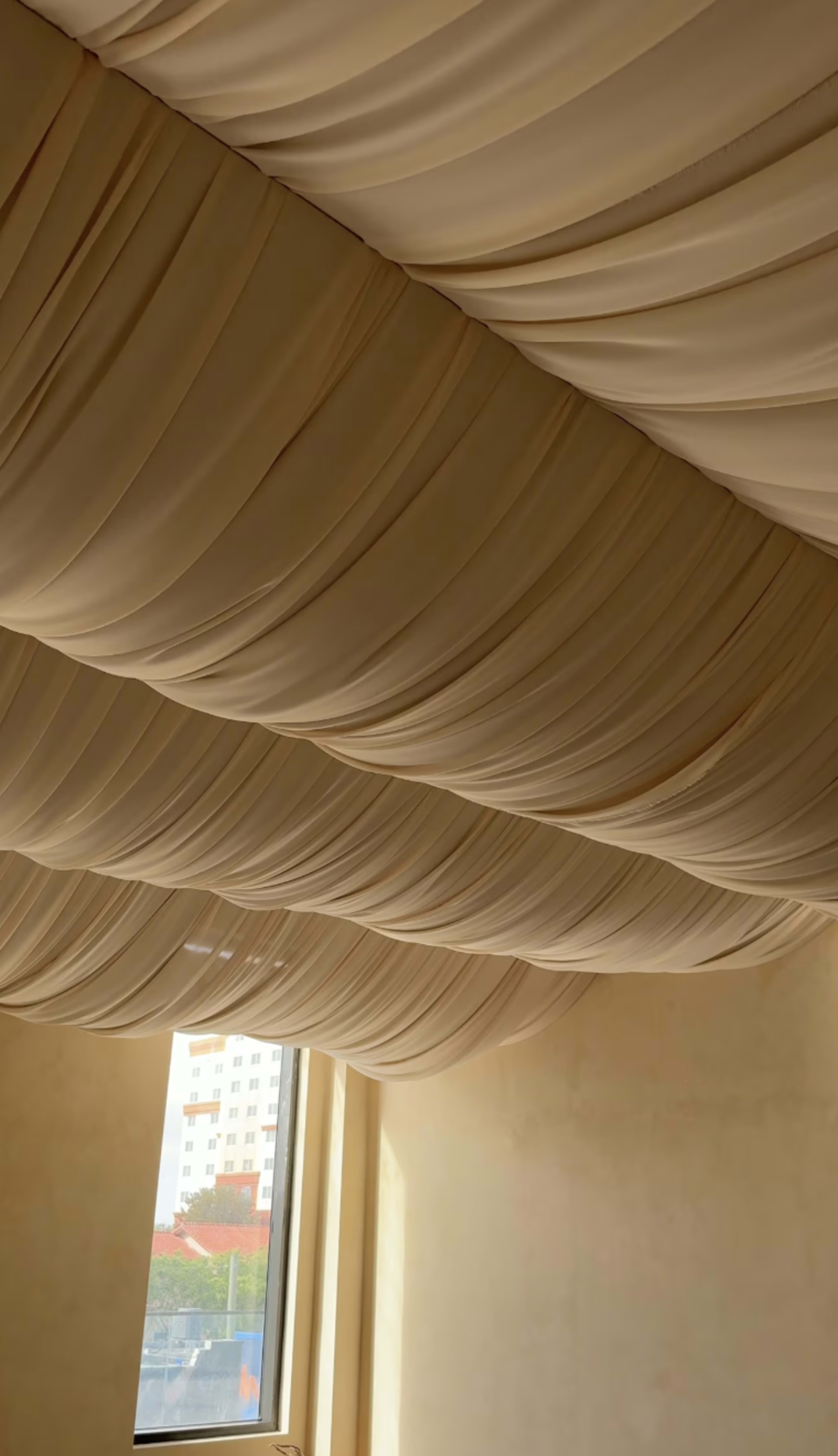 The image shows a draped ceiling of fabric in a neutral color, with a window revealing a view of buildings outside.