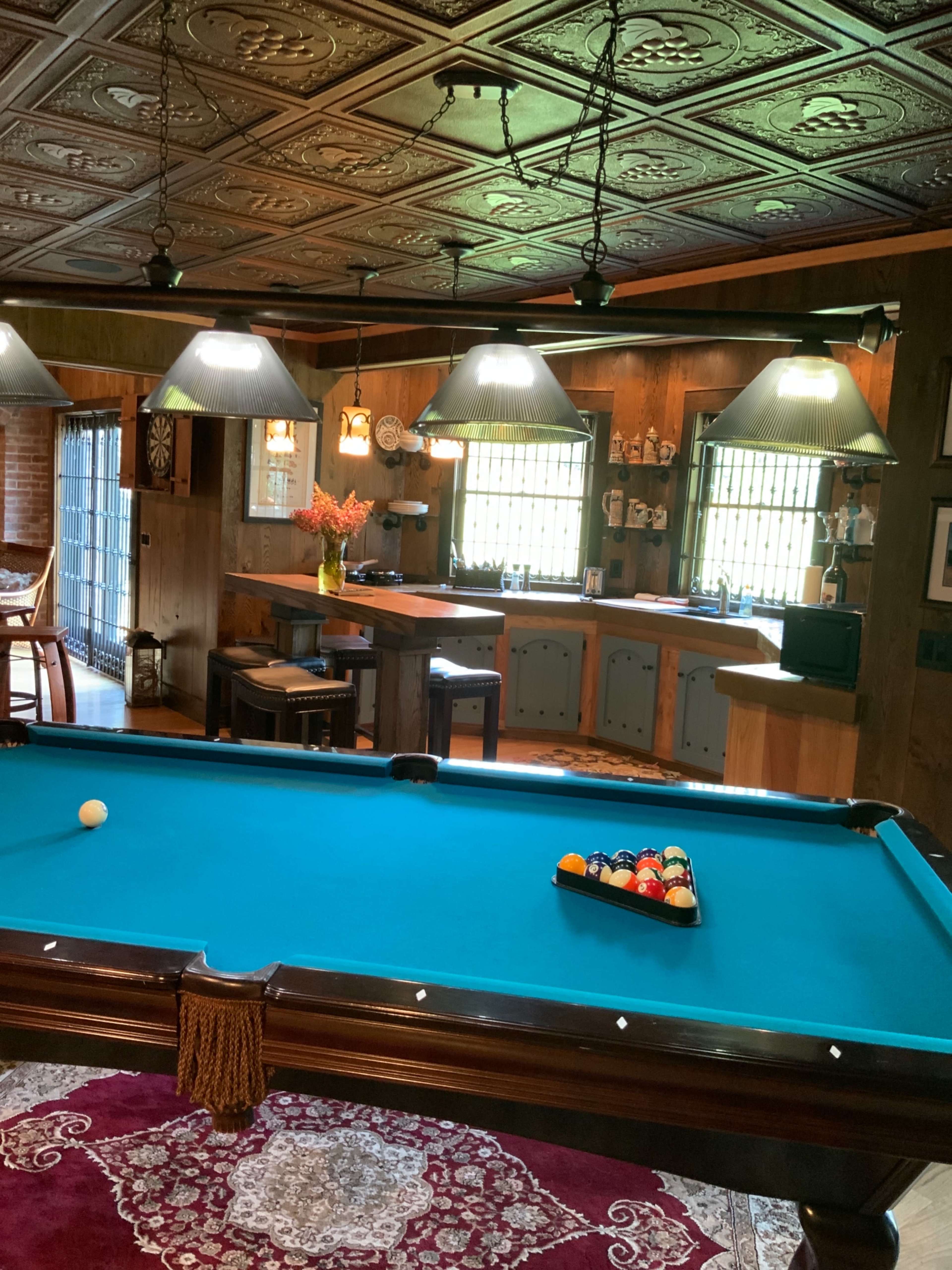 A game room with a pool table, a bar area in the background, and decorative lighting throughout.