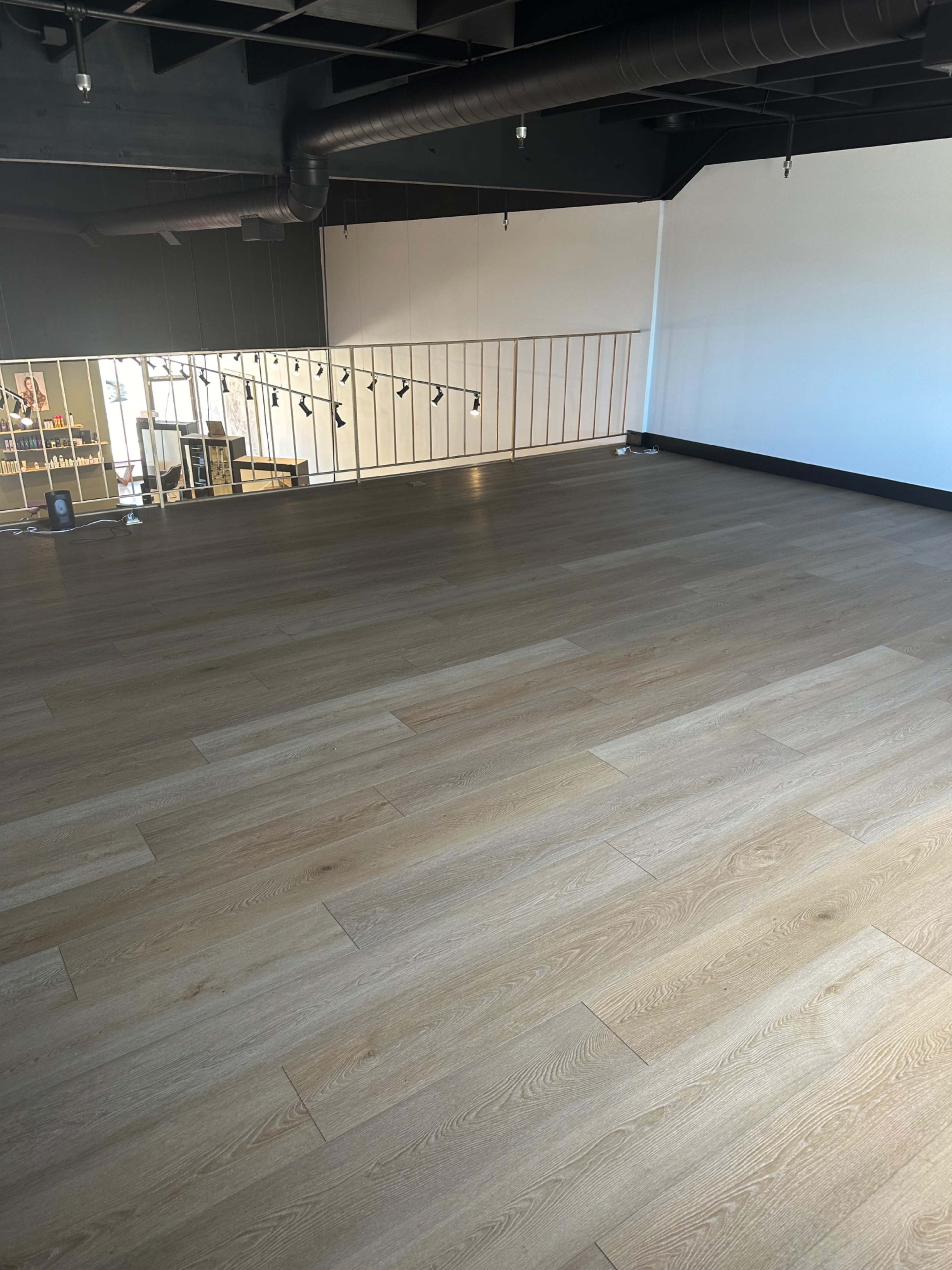 The image shows an empty room with wooden flooring and a railing along one side of the space.