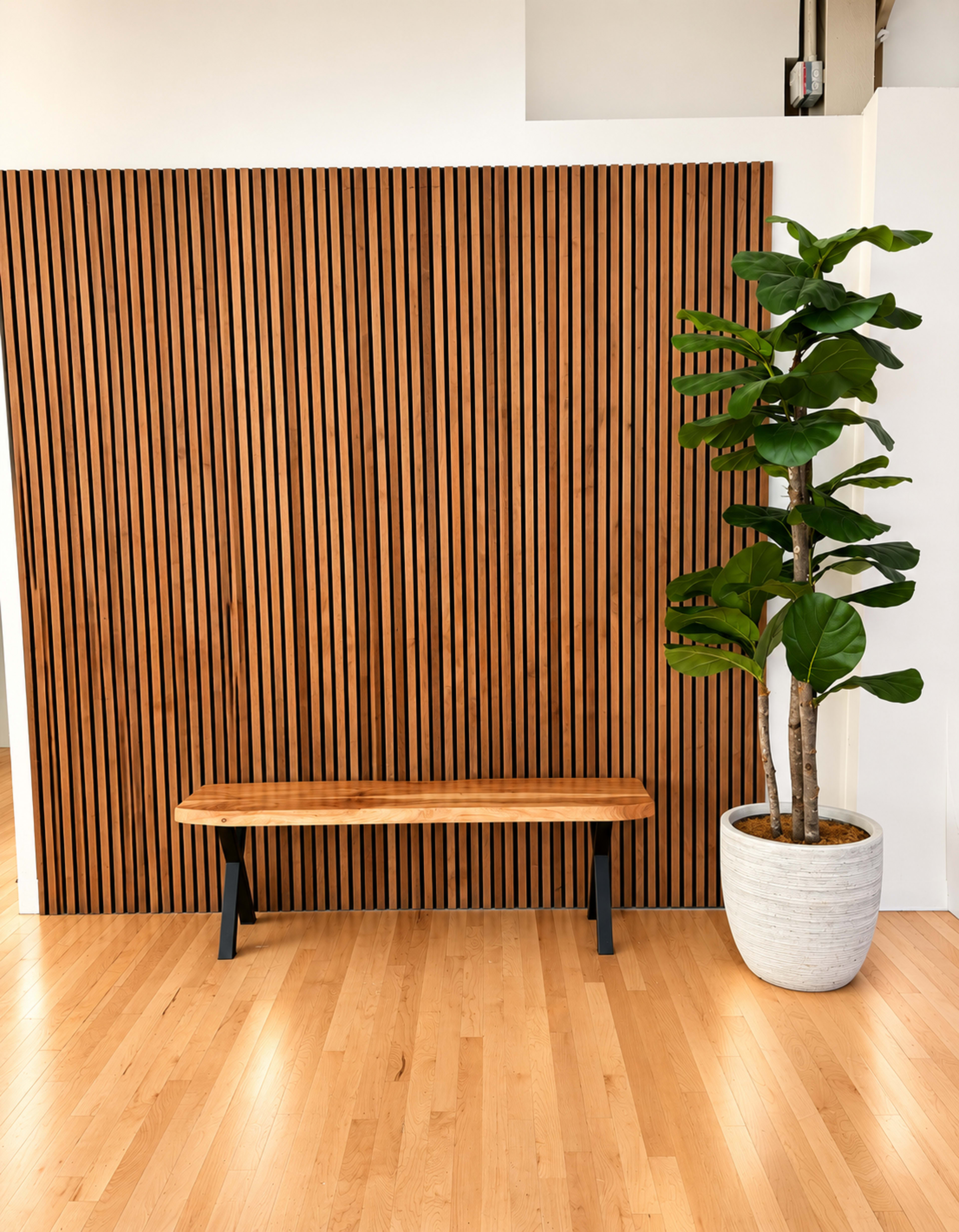A wooden bench sits in front of a slatted wooden wall beside a potted plant in a white planter.