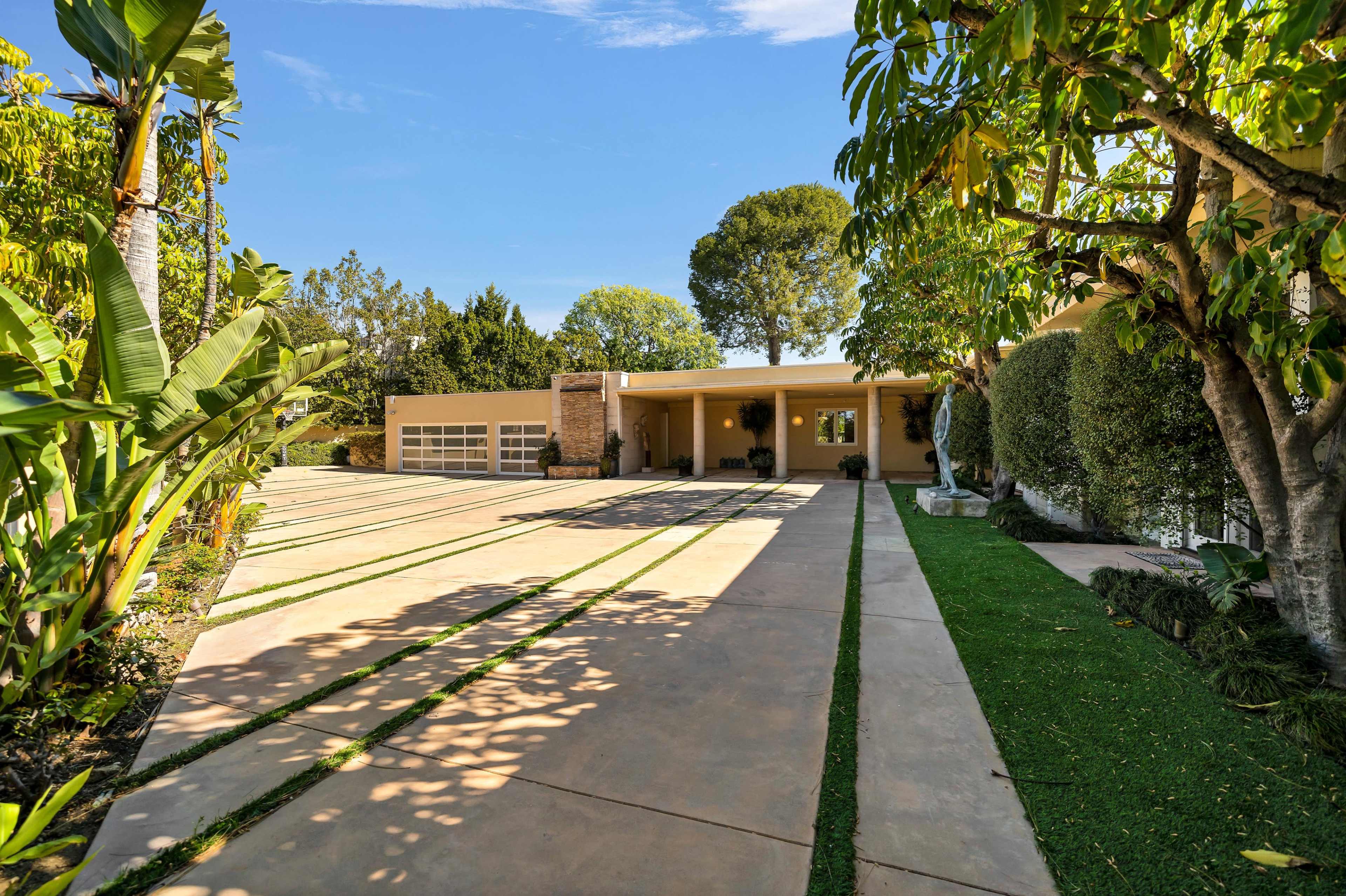 A modern house with a wide driveway, bordered by greenery and trees.