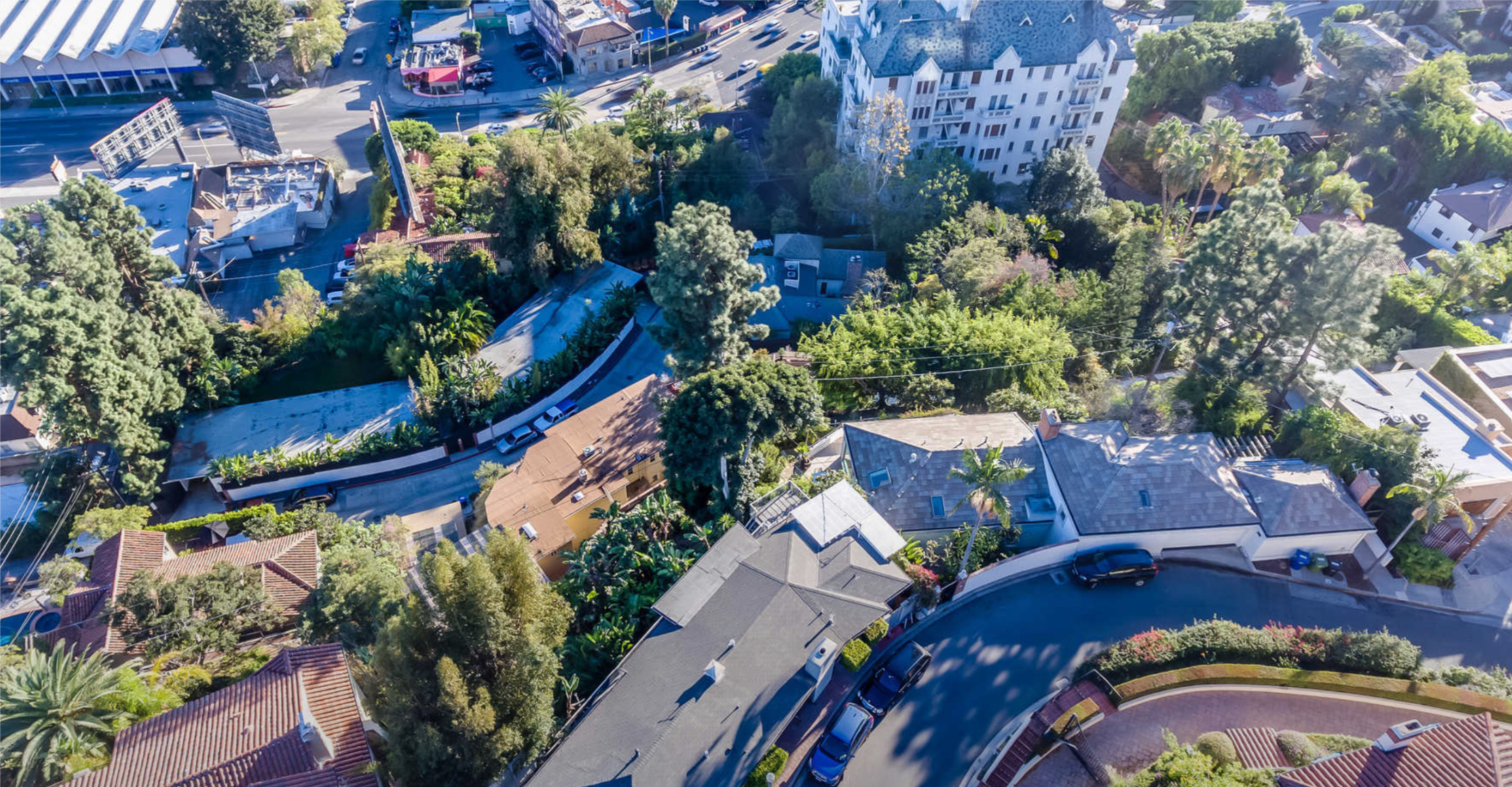 An aerial view captures a residential neighborhood featuring various homes, lush greenery, and winding streets amidst urban infrastructure.