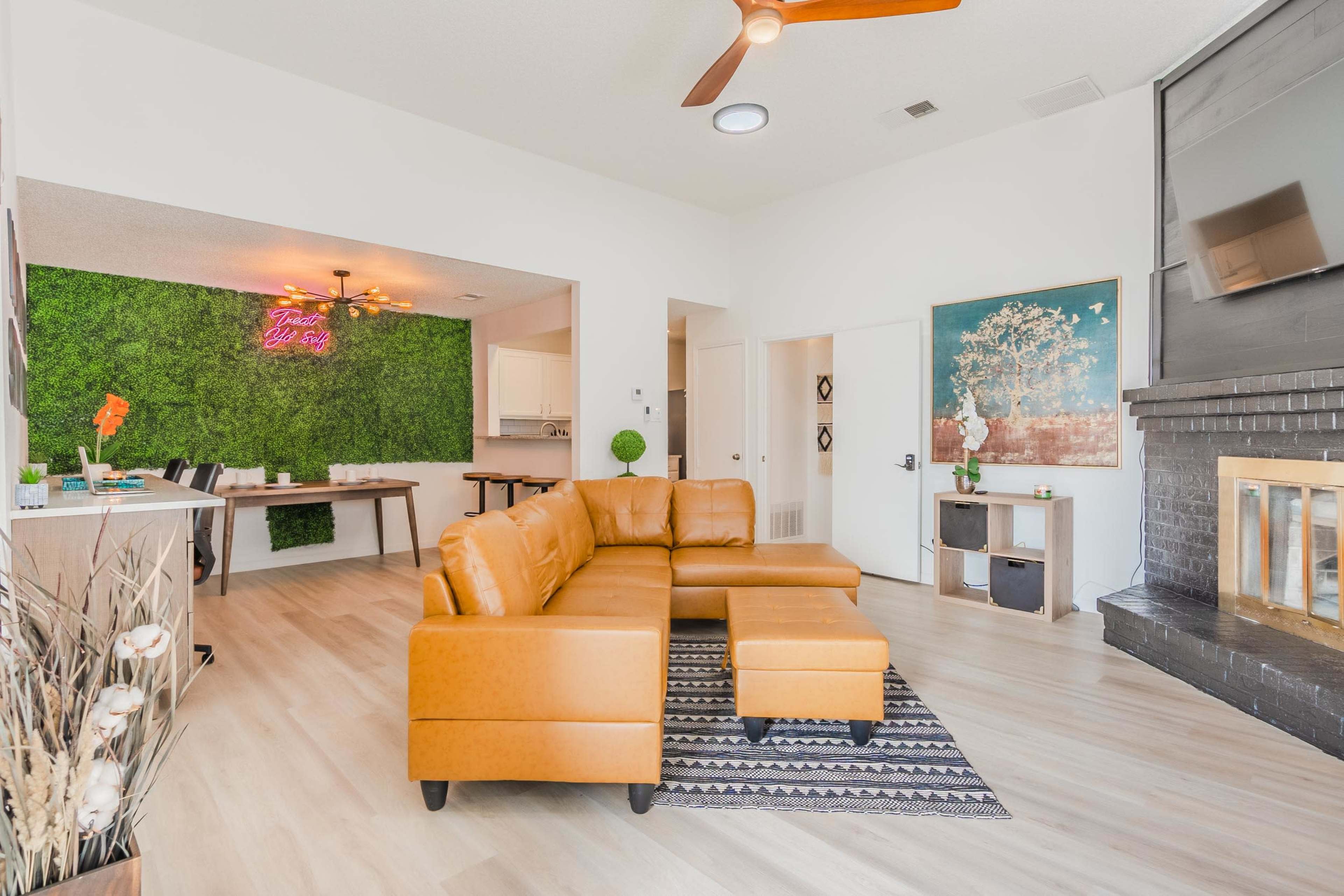 The living area features a yellow-orange sectional sofa, a green accent wall, a fireplace, and a workspace with a table and chairs.