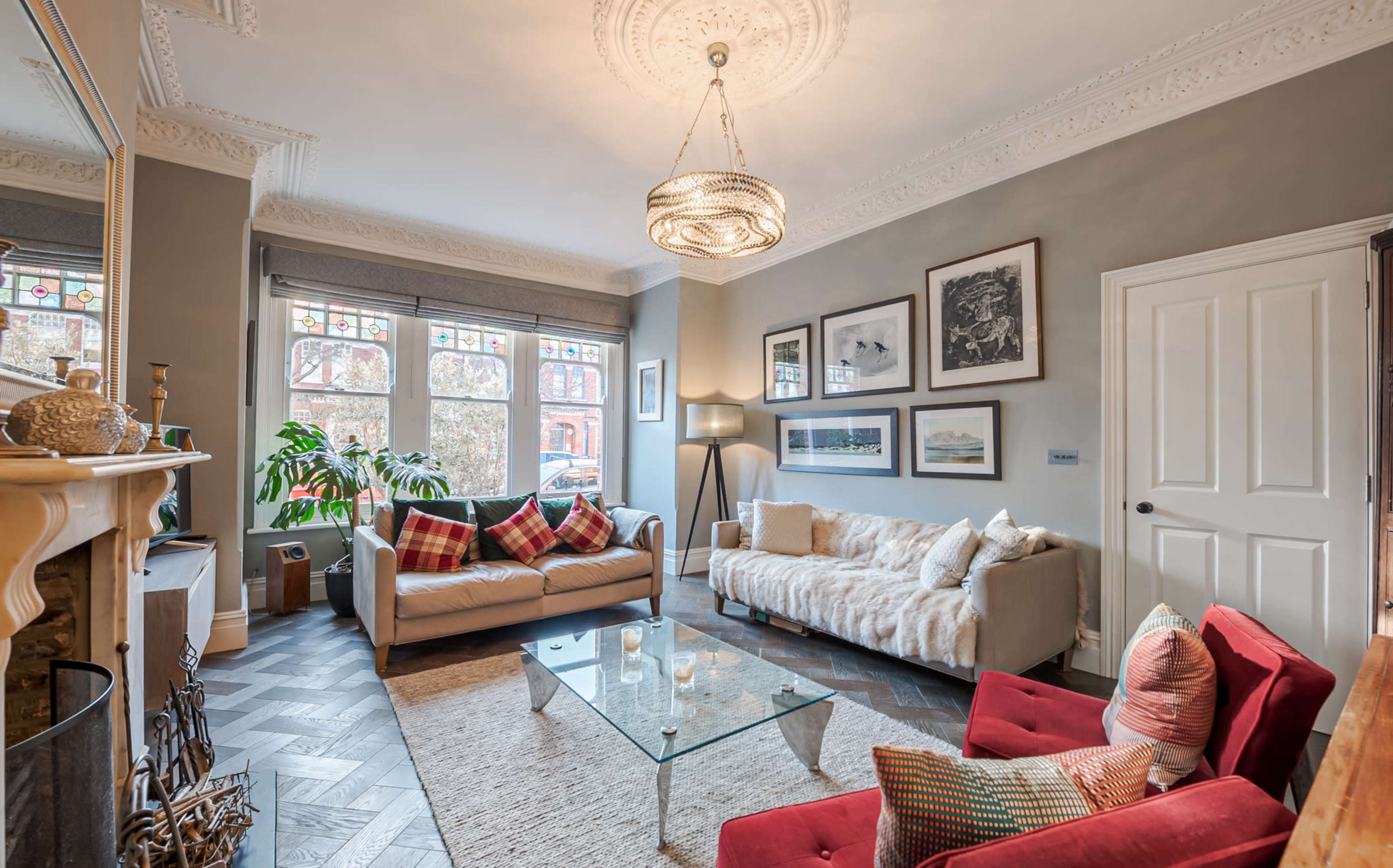 A living room with a glass coffee table, red and beige seating, and large windows adorned with decorative stained glass.
