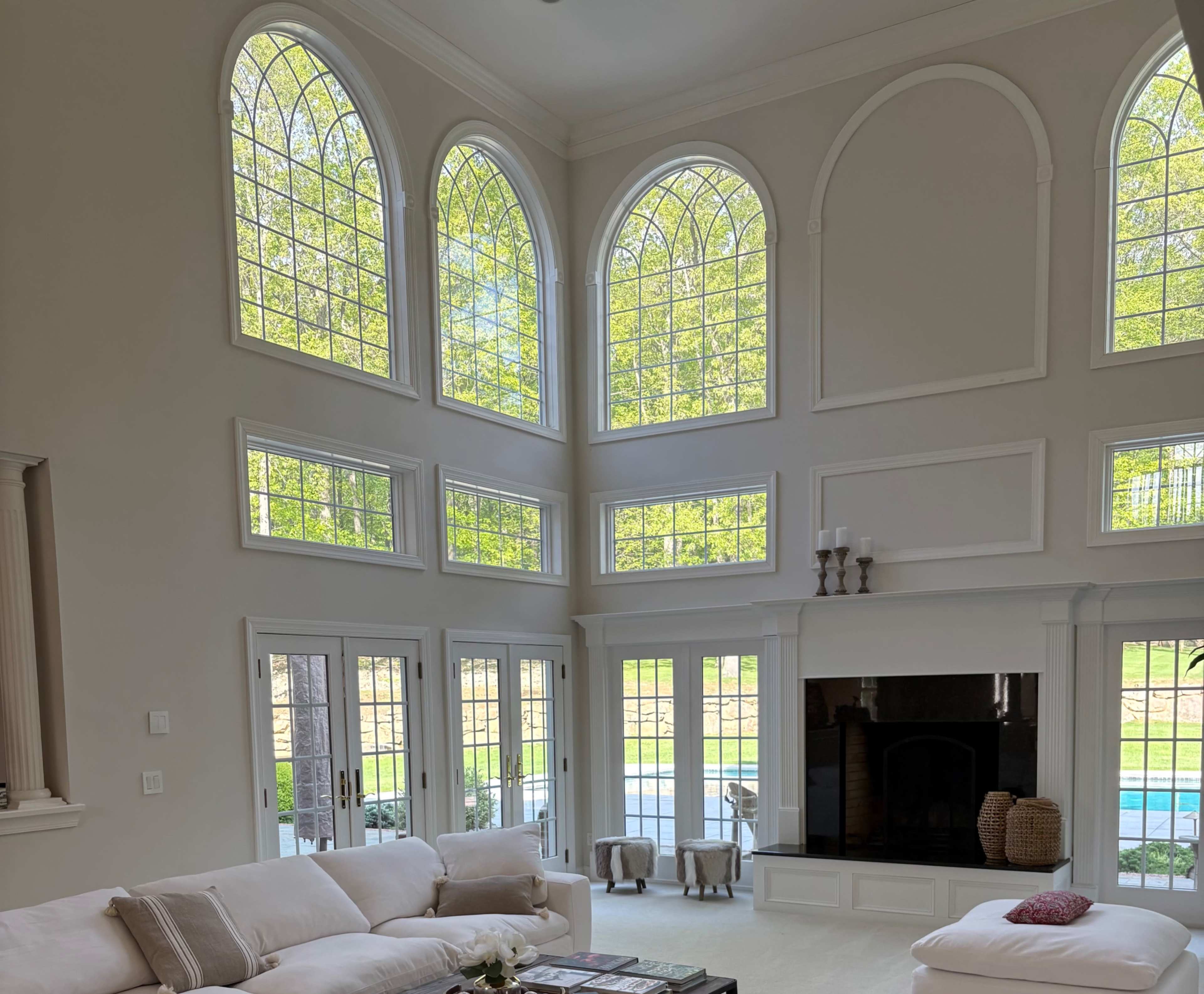 The image shows a spacious living room with large arched windows that provide natural light, a white sofa, and a fireplace.