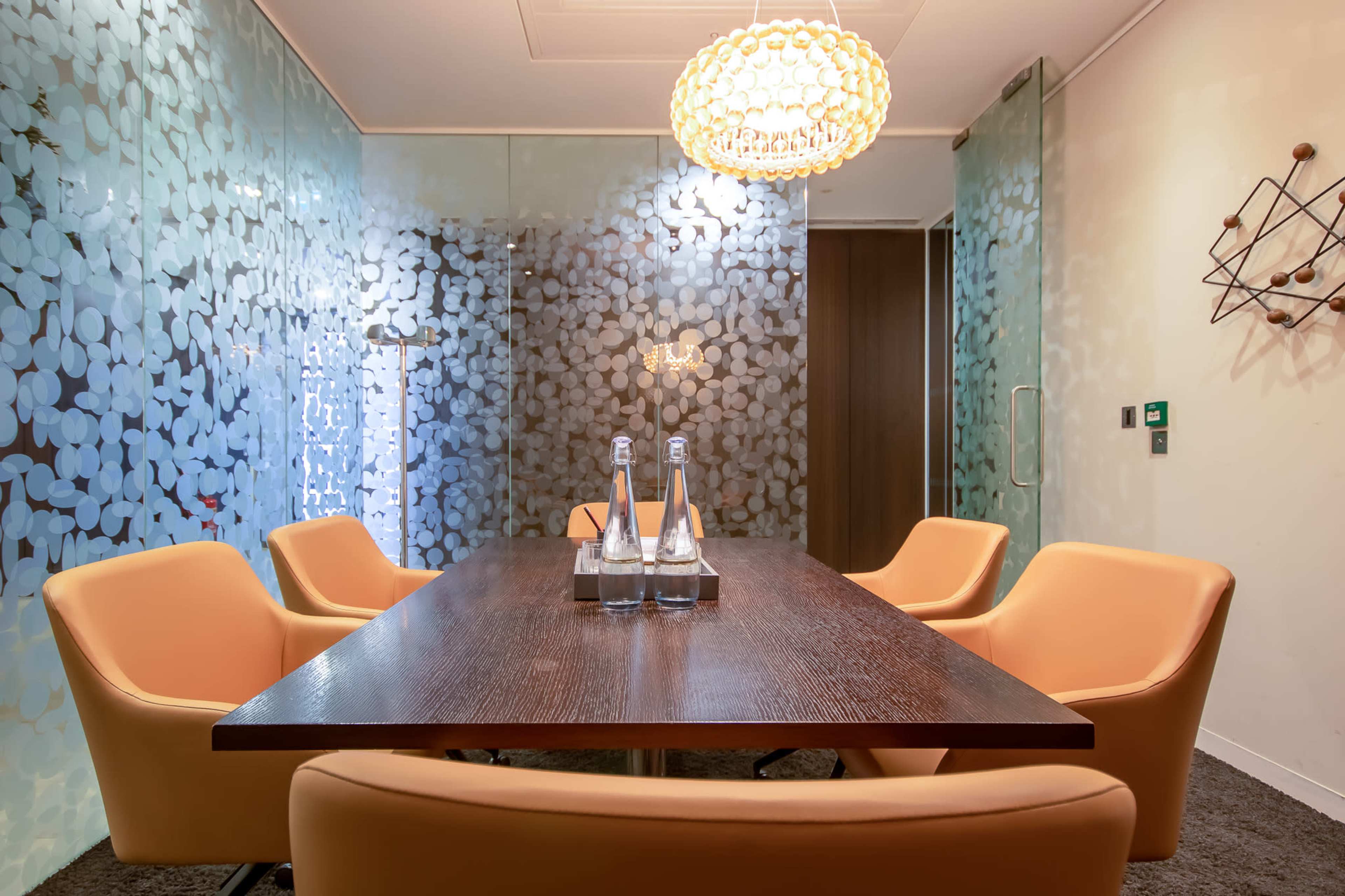 A modern conference room with a wooden table, orange chairs, and decorative glass walls featuring leaf patterns.