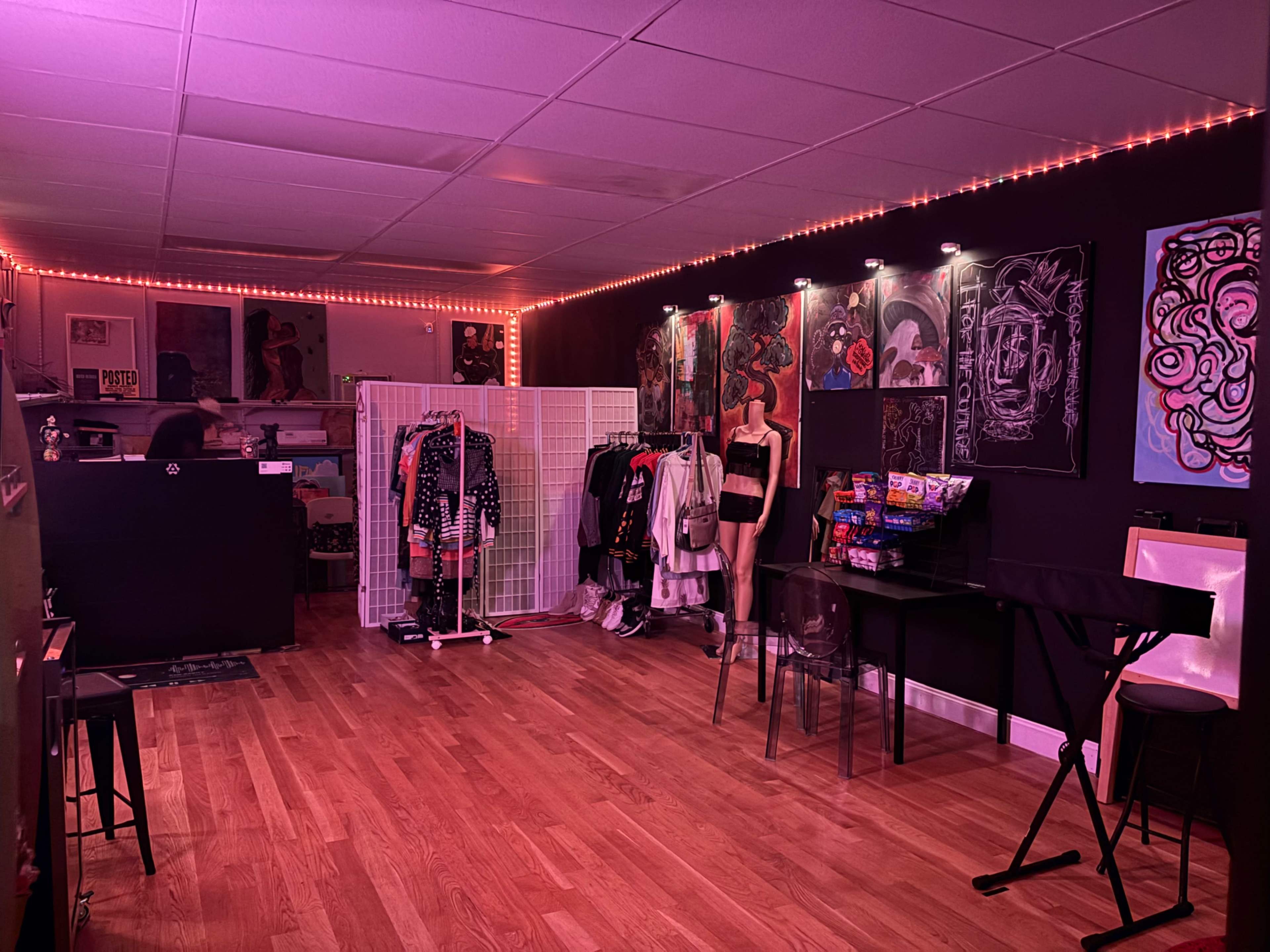 The image shows an interior of a boutique with pink lighting, displaying racks of clothing and art on the walls.