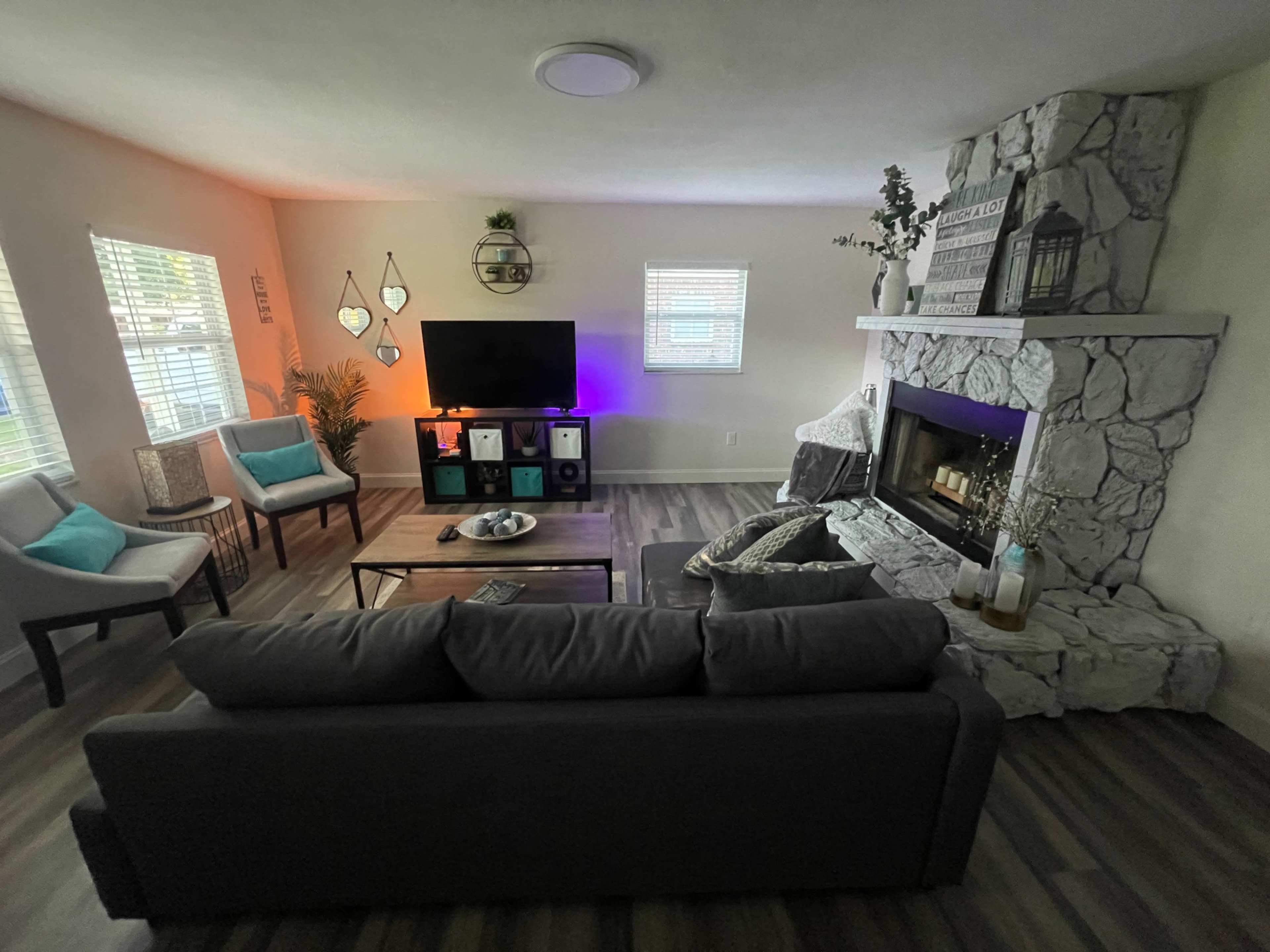 The living room features a stone fireplace, a television on the wall, and seating arranged around a coffee table.
