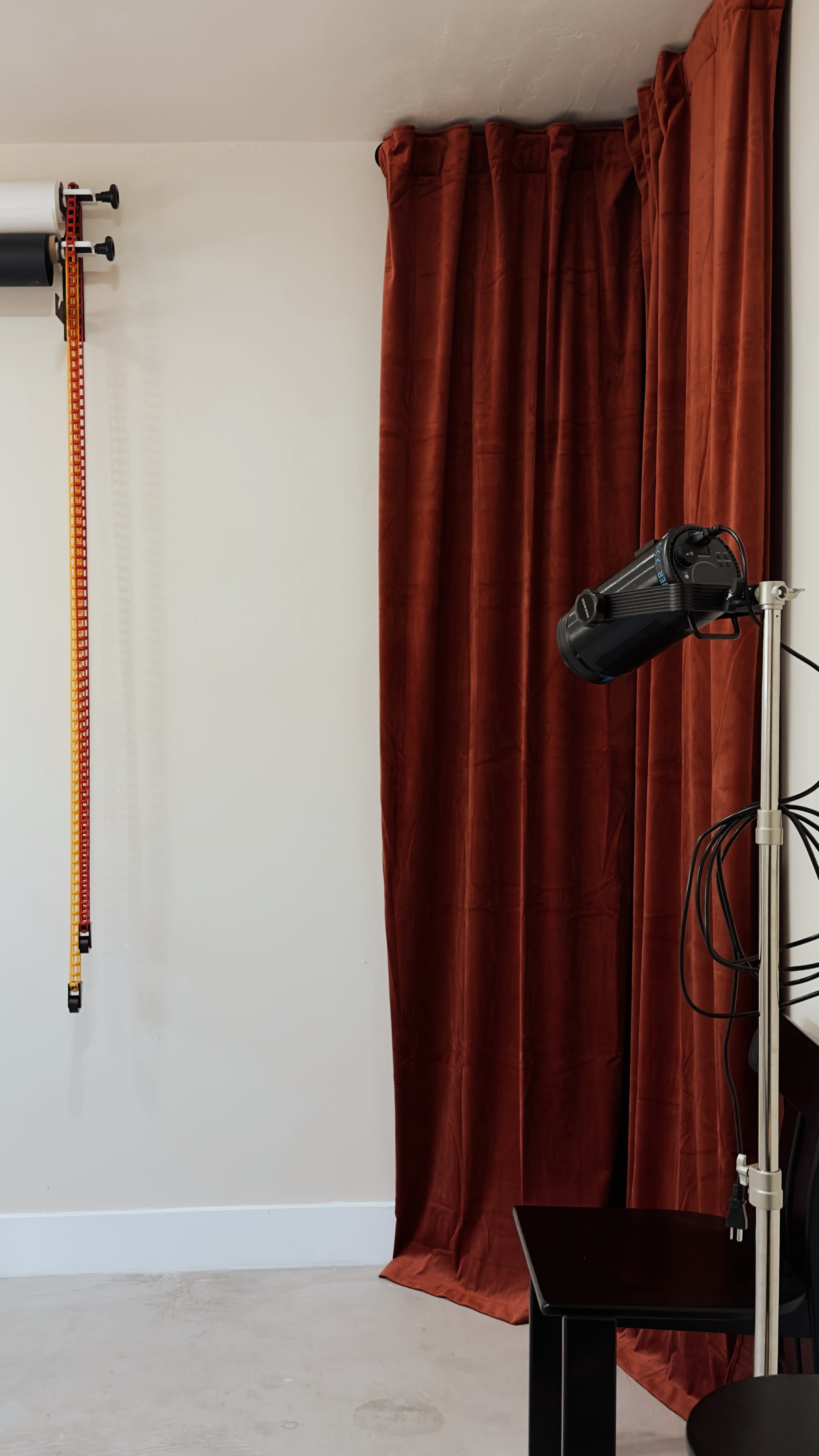 A room with a wall-mounted device, a curtain, and a floor lamp with multiple cords on a dark surface.