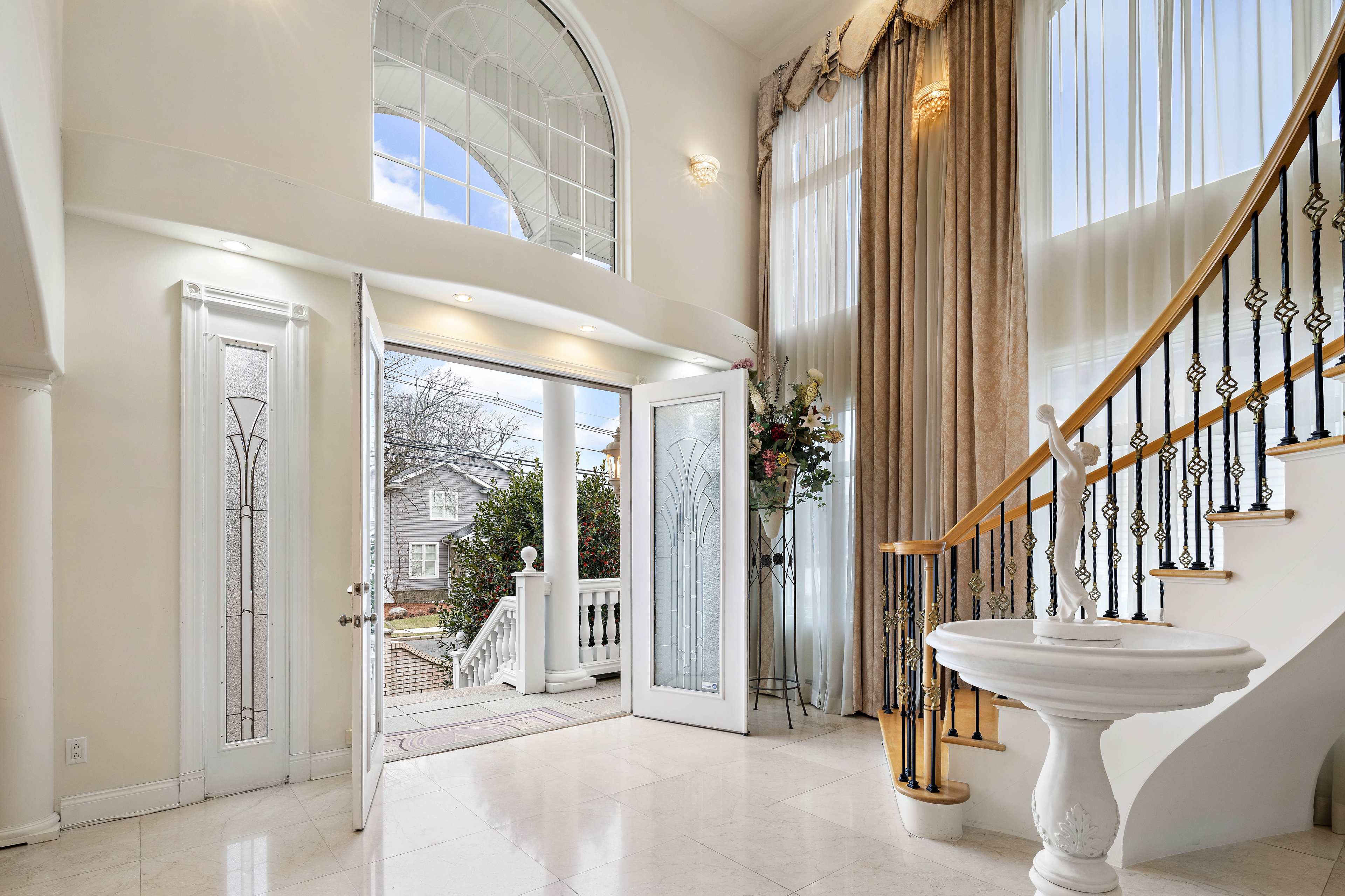A spacious entryway features double glass doors opening to the outside, large windows allowing natural light, and a staircase leading to the upper floor.