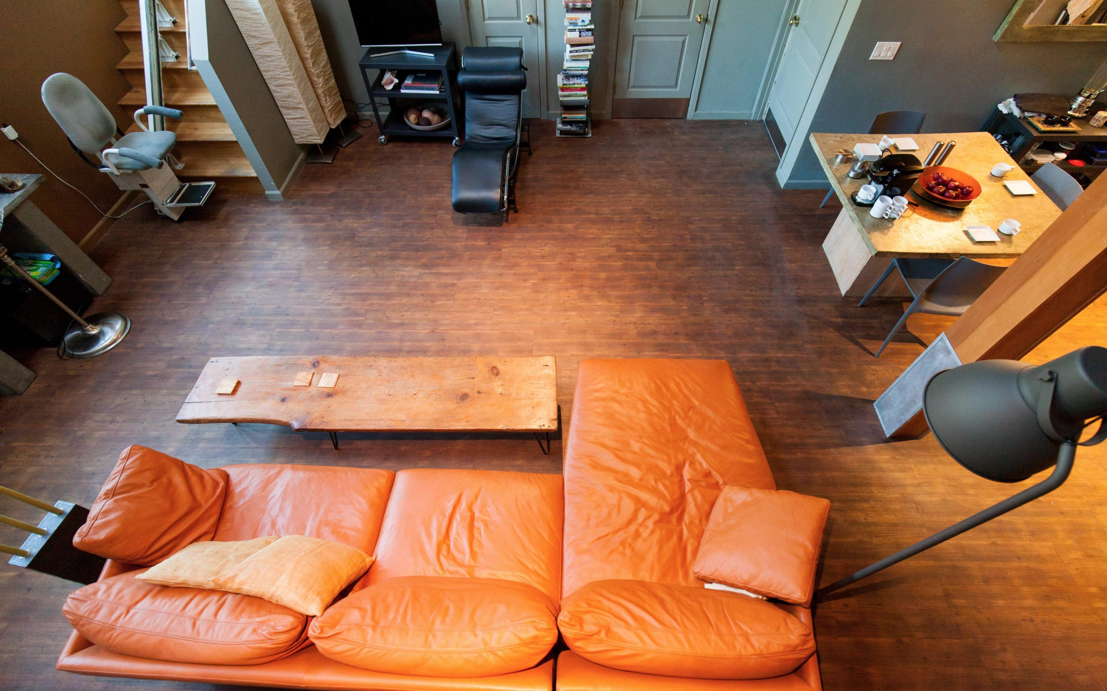 A spacious living area featuring an orange leather couch, a wooden coffee table, a dining area, and a staircase in the background.