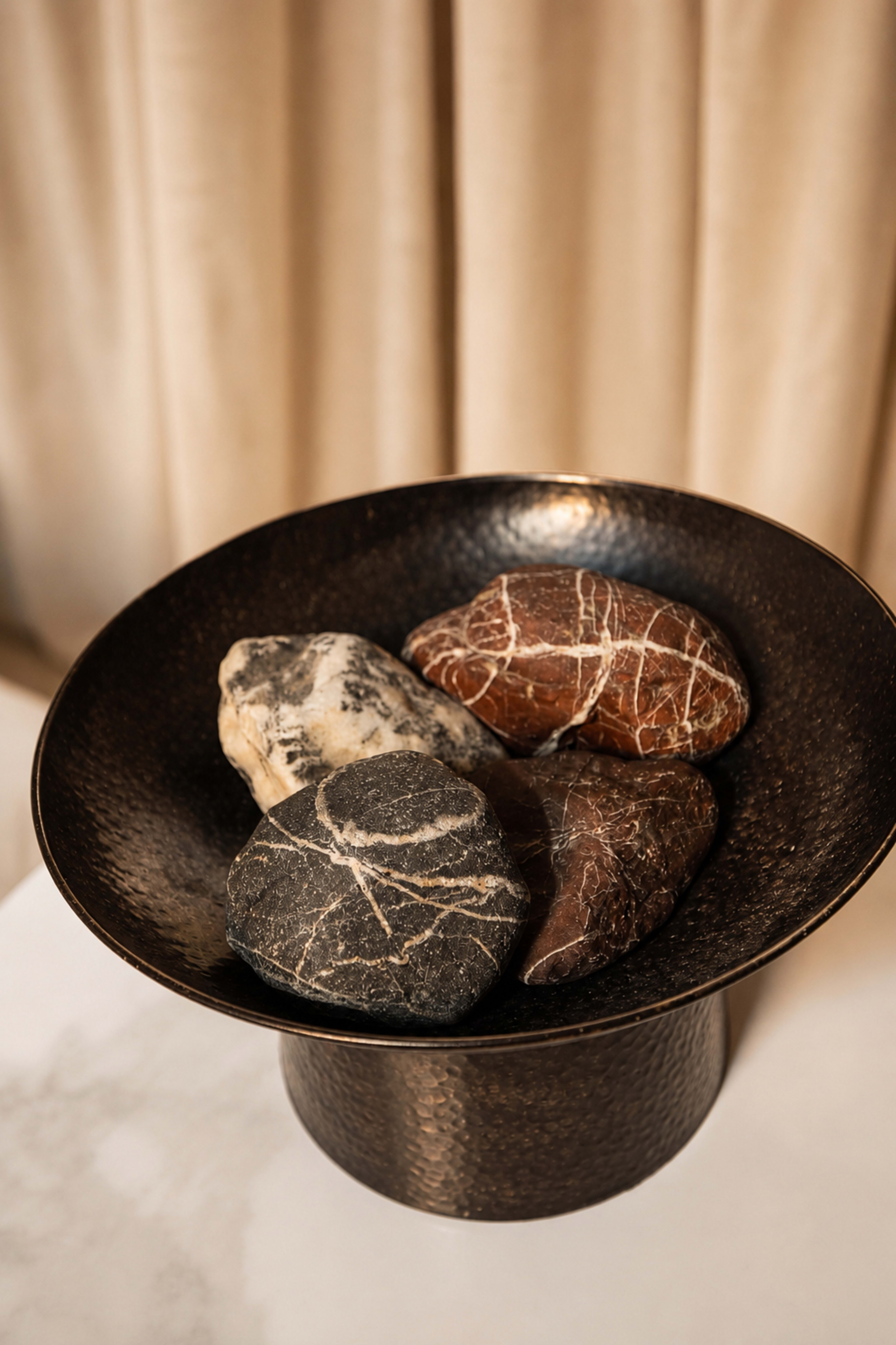 A dark bowl with a textured surface holds four decorative stones of different colors and patterns.
