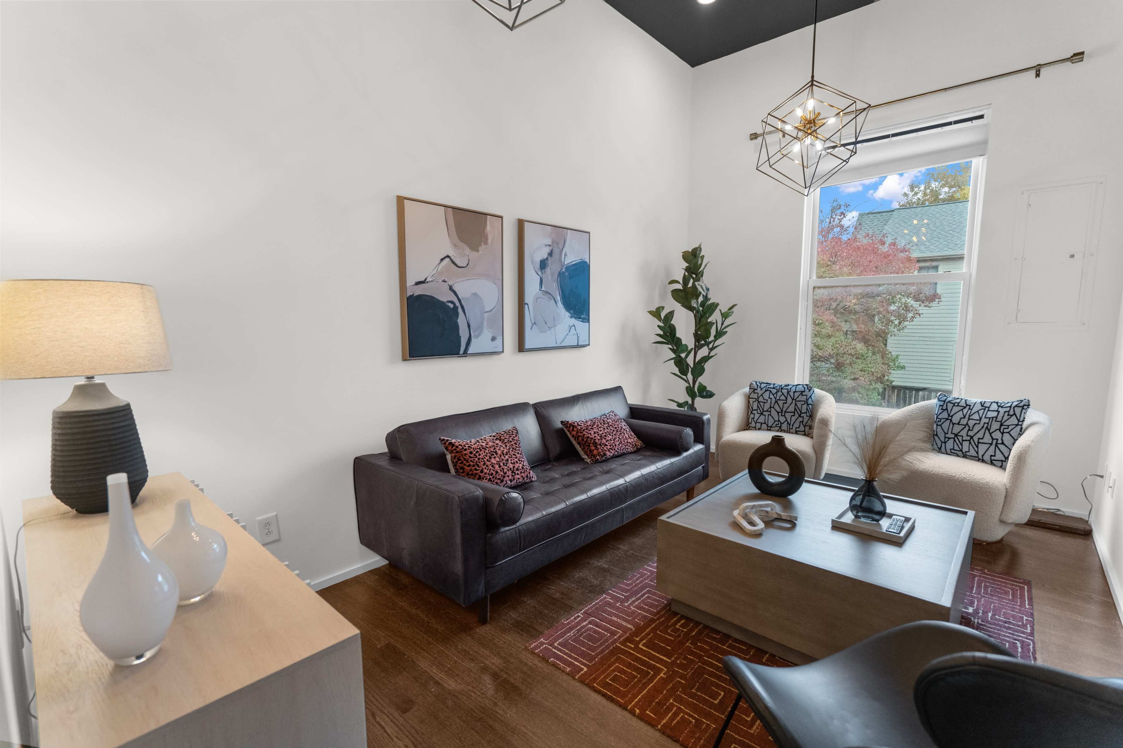 A modern living room featuring a dark sofa, light armchairs, a coffee table, and two framed artworks on the wall.