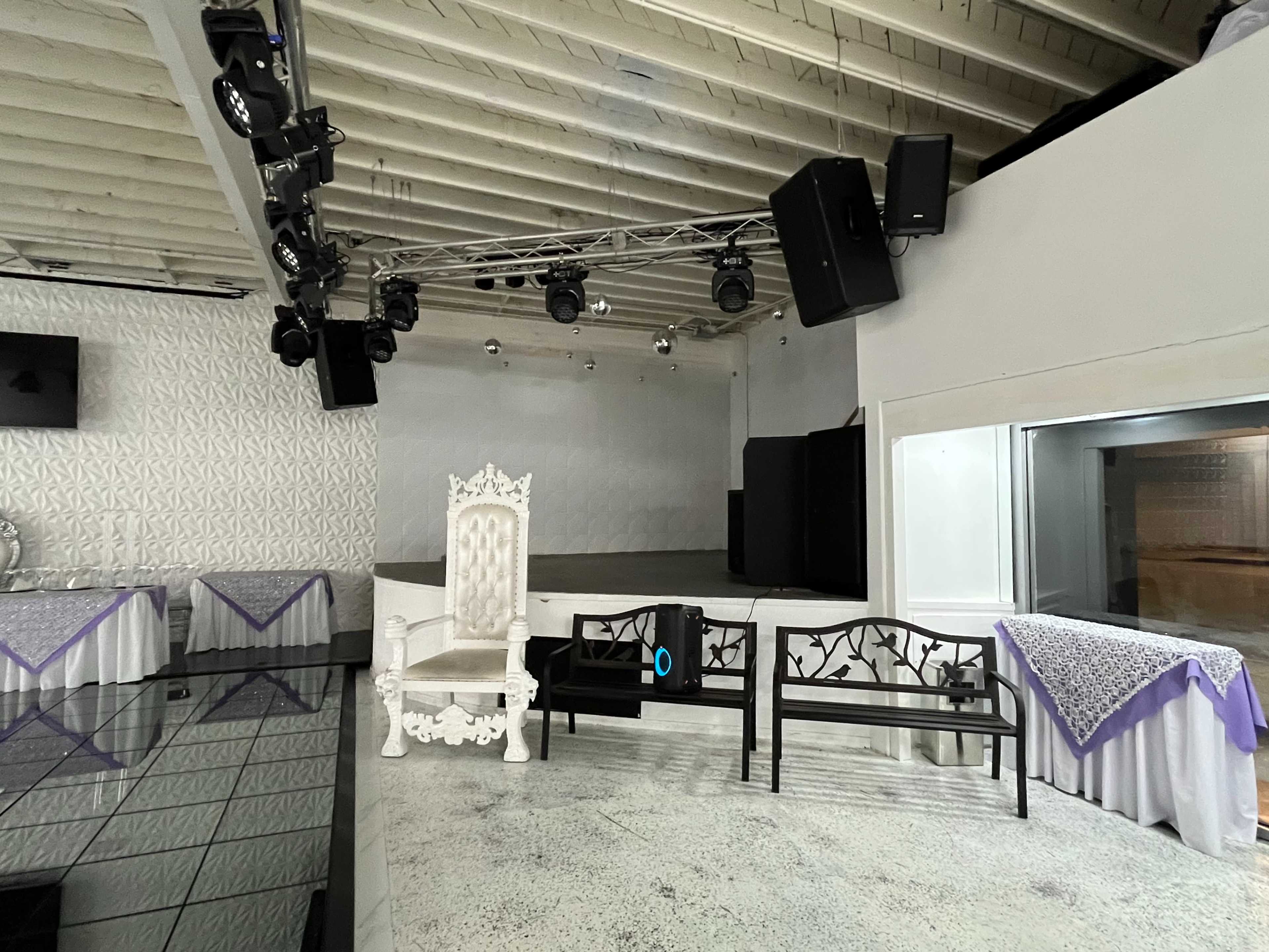 The image shows a spacious, modern event venue with a stage, decorative lighting, and seating arranged around the area.